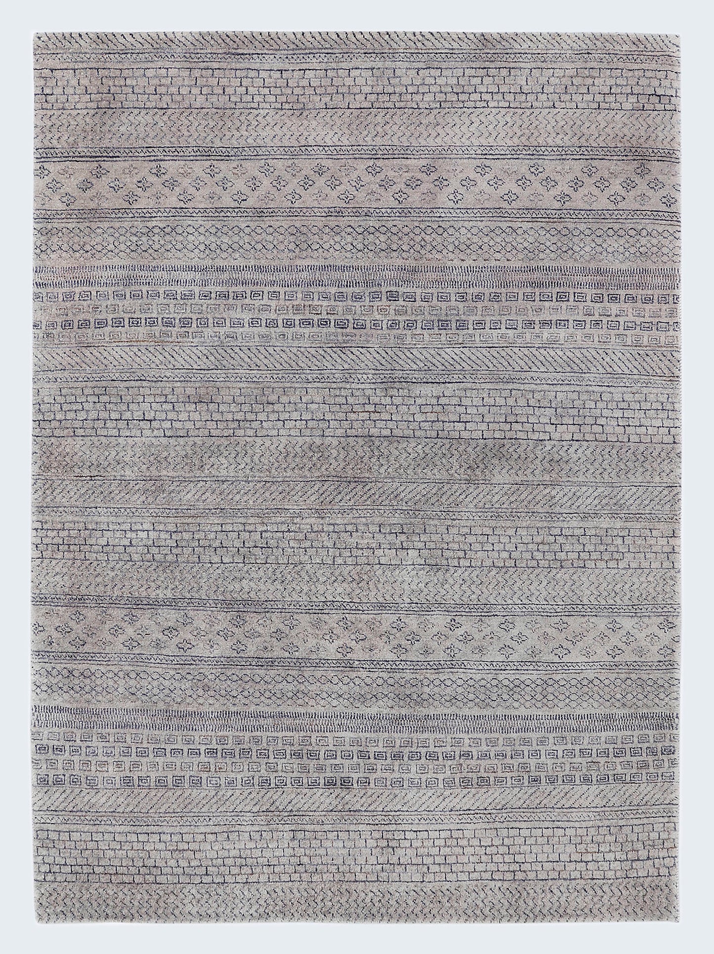 A full view of a plush, hand-knotted Gabbeh rug from the Aatish collection, featuring horizontal bands of charcoal geometric tribal motifs over a light stony-grey wool foundation.