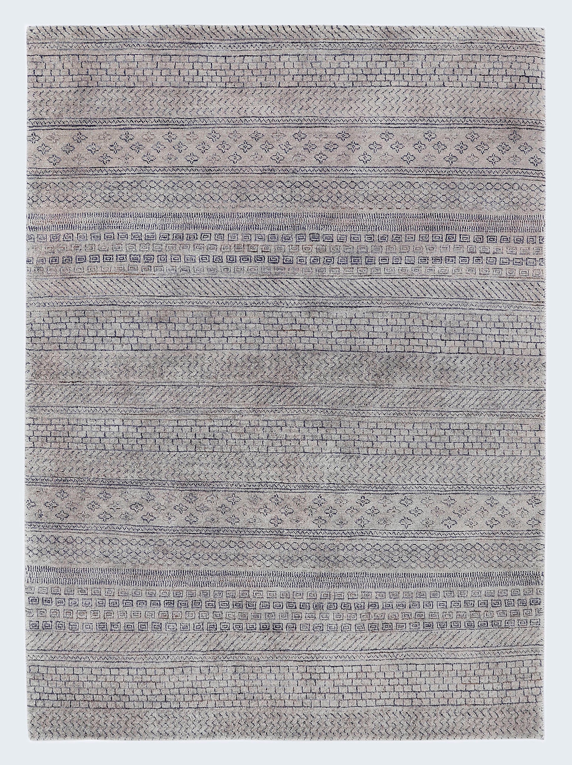 A full view of a plush, hand-knotted Gabbeh rug from the Aatish collection, featuring horizontal bands of charcoal geometric tribal motifs over a light stony-grey wool foundation.