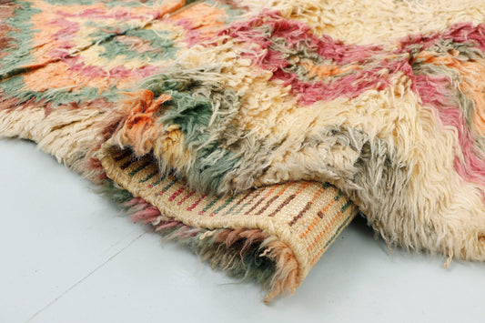 A close-up highlighting the plush, thick shag texture of a cream Moroccan rug, detailing the beautifully blended, feathery edges of the rose and sage green wool within a geometric diamond motif.