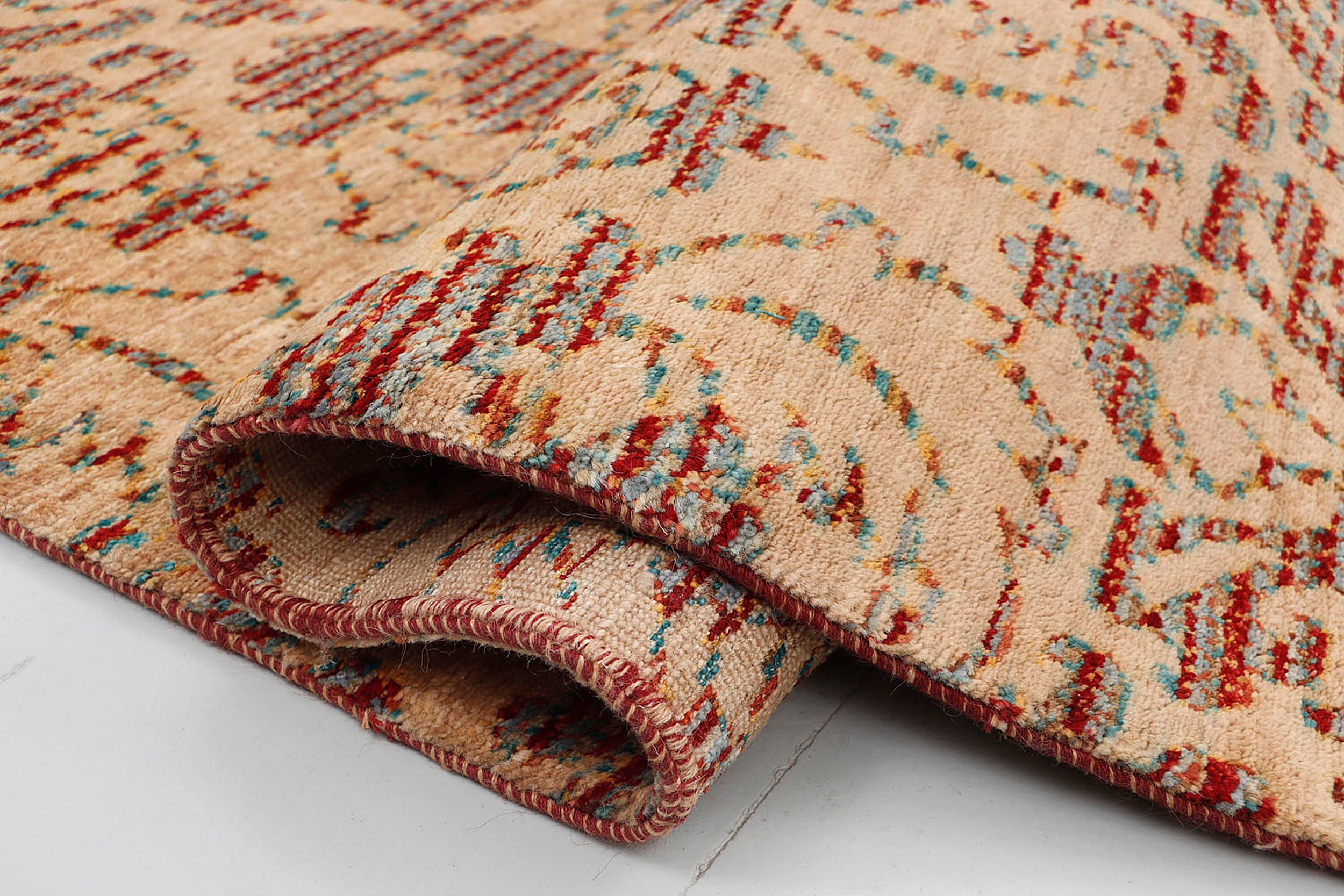 A close-up of a crisp, medium-pile hand-knotted wool rug highlighting the complex artisan technique of using terracotta and teal tie-dyed yarns to form traditional repeating motifs.