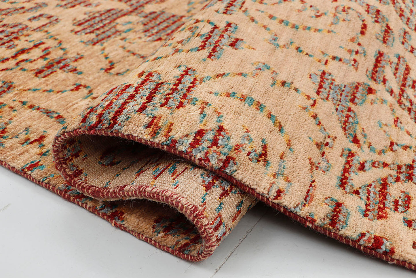 A close-up of a crisp, medium-pile hand-knotted wool rug highlighting the complex artisan technique of using terracotta and teal tie-dyed yarns to form traditional repeating motifs.