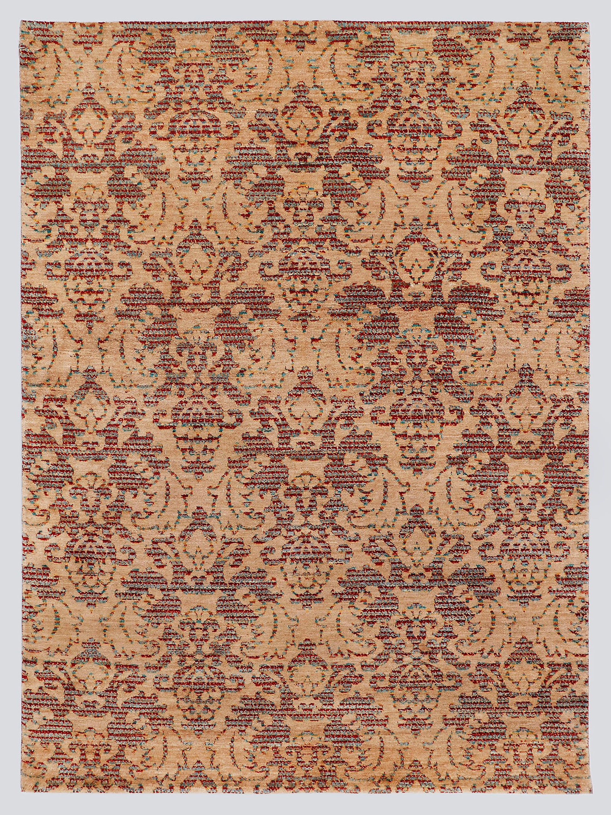 A full view of a modern transitional hand-knotted rug from the Nomad Series, featuring a repeating classical palmette pattern rendered in warm, tie-dyed wool over an amber-sand foundation.
