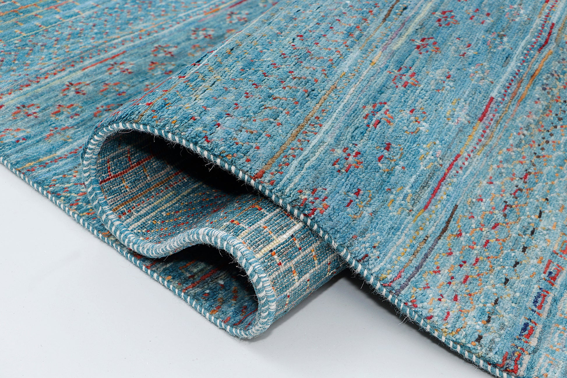 A close-up of a thick-pile wool rug highlighting the dense texture and the rhythmic, script-like rows of colorful nomadic symbols against an aquatic blue-green background.