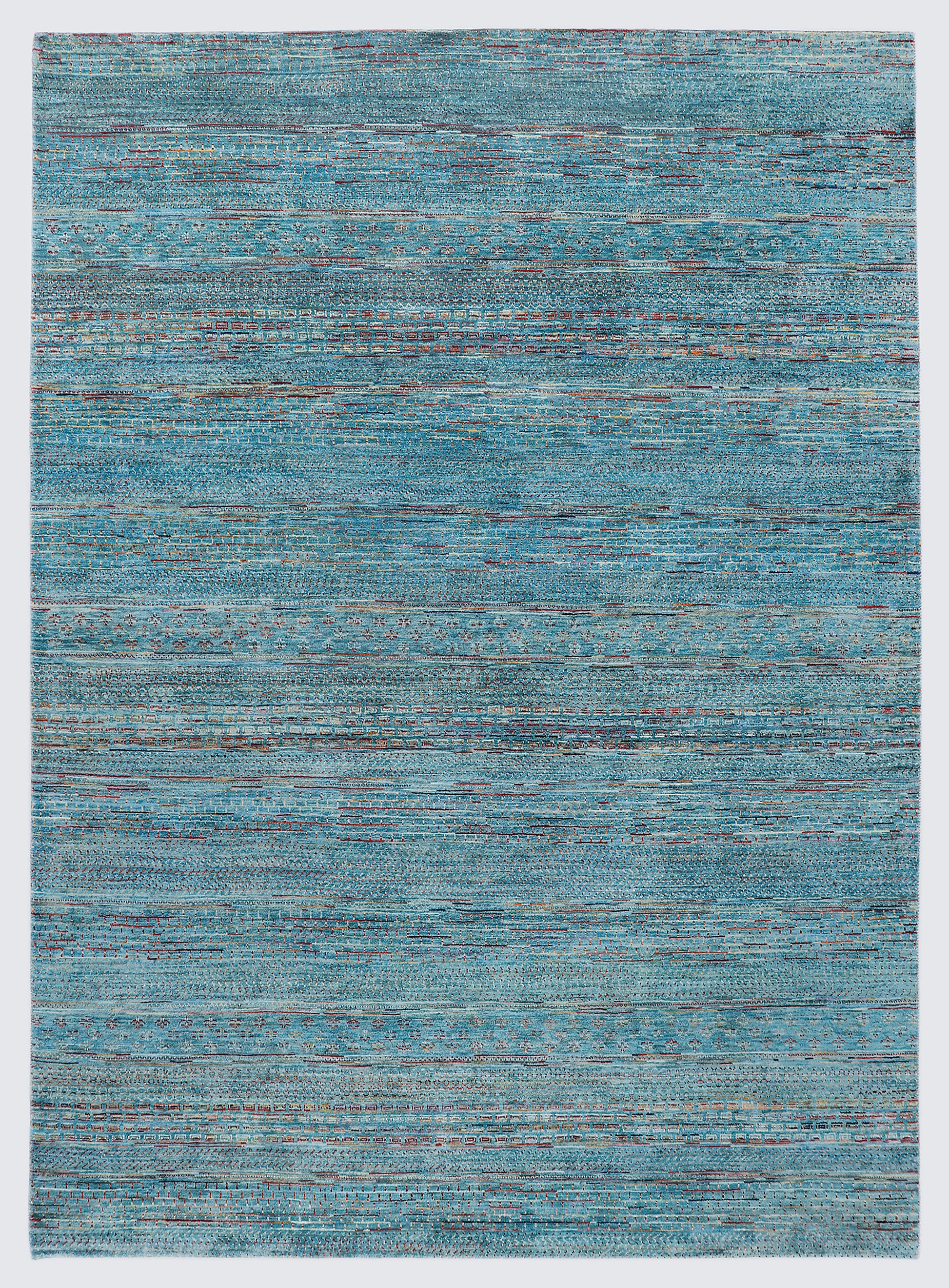 A full view of a vibrant hand-knotted Gabbeh rug from the Aatish collection, featuring horizontal bands of saffron and ivory tribal motifs over a striated sea blue-green foundation.