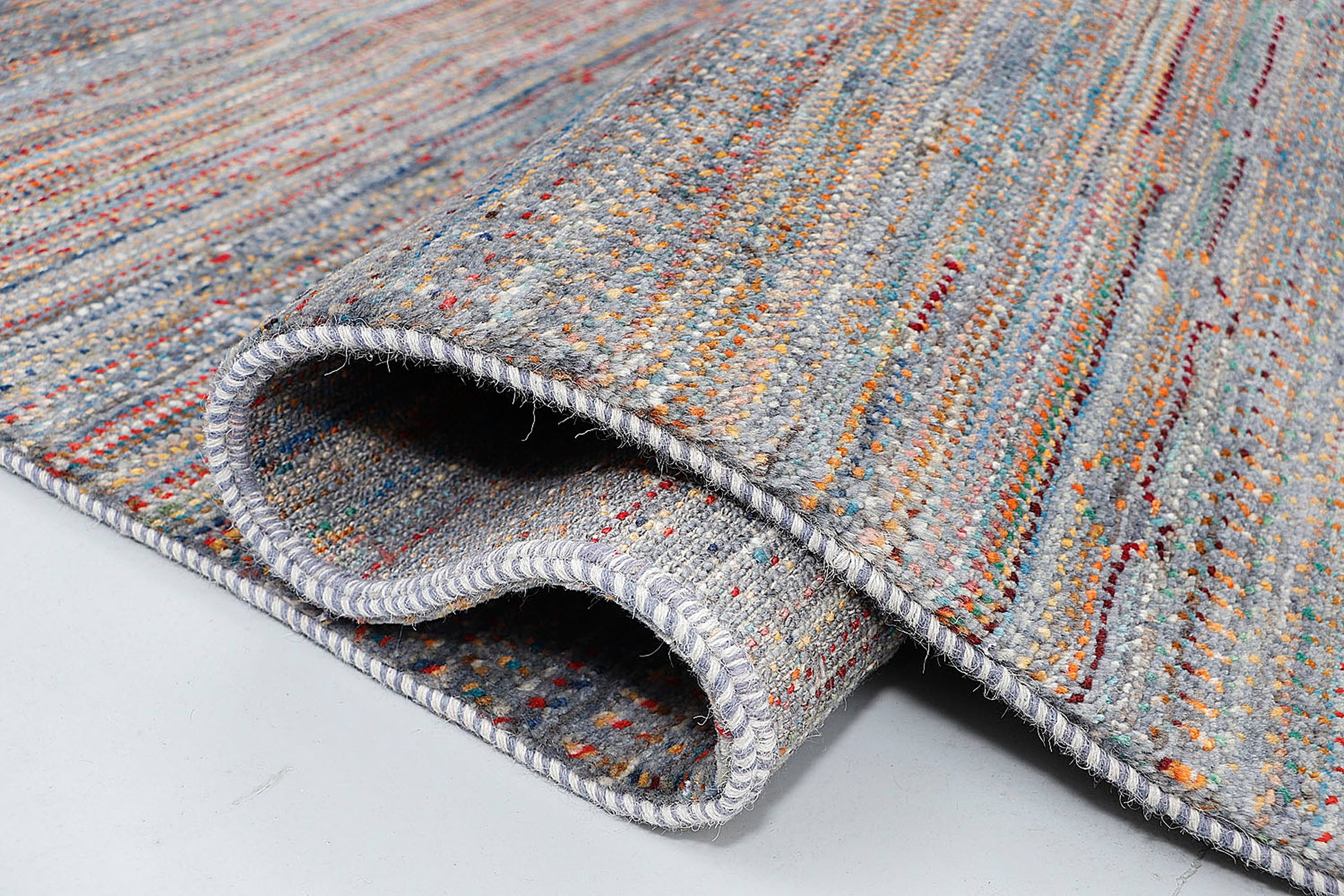 A high-resolution close-up of a double-knot wool rug highlighting the silver-grey "abrash" texture and the unique ombré effects of the multi-colored elements.