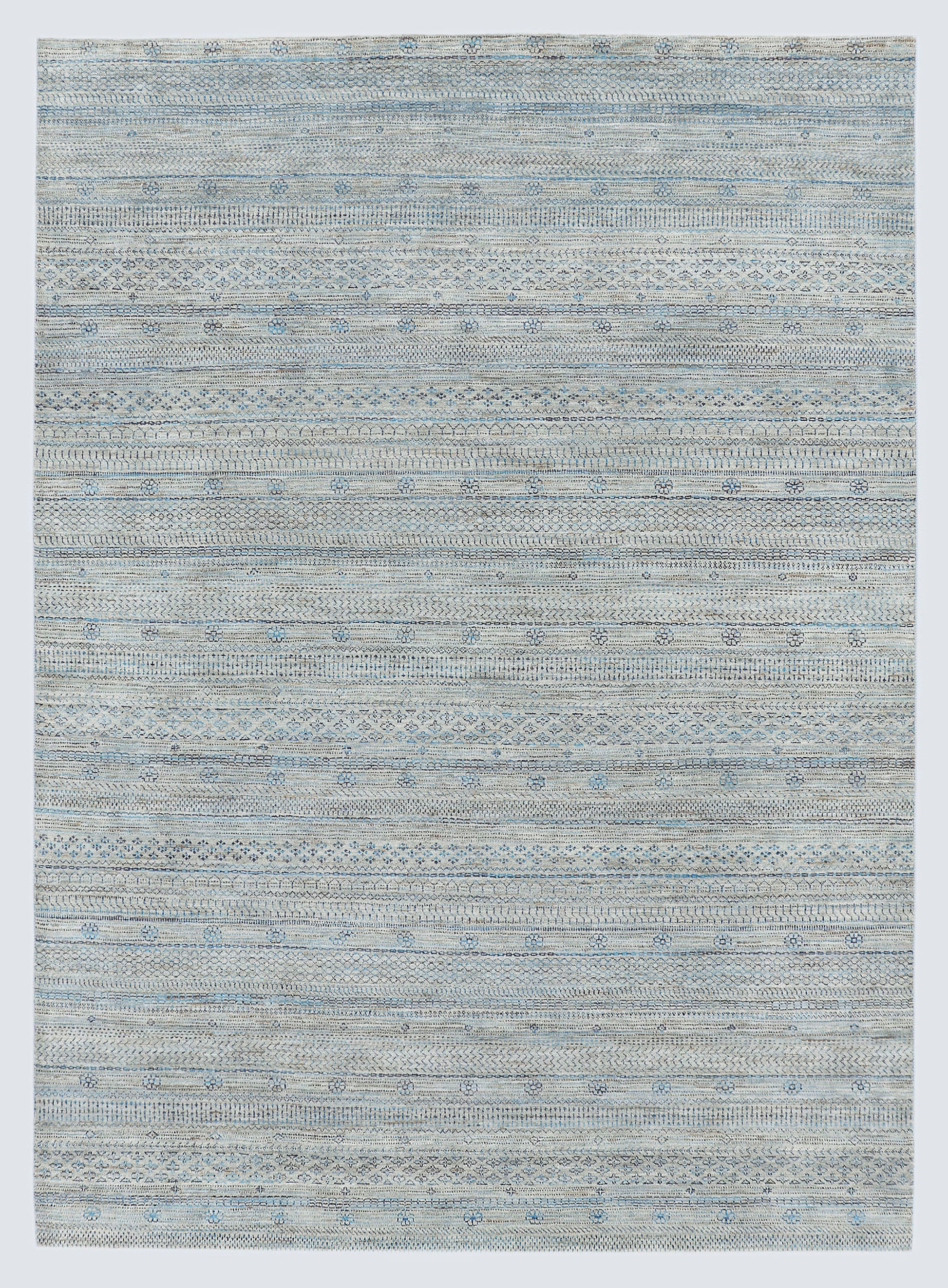 A full view of a sophisticated silver-grey hand-knotted Gabbeh rug from the Aatish collection, featuring horizontal bands of tie-dyed tribal motifs over a textured, natural wool foundation.