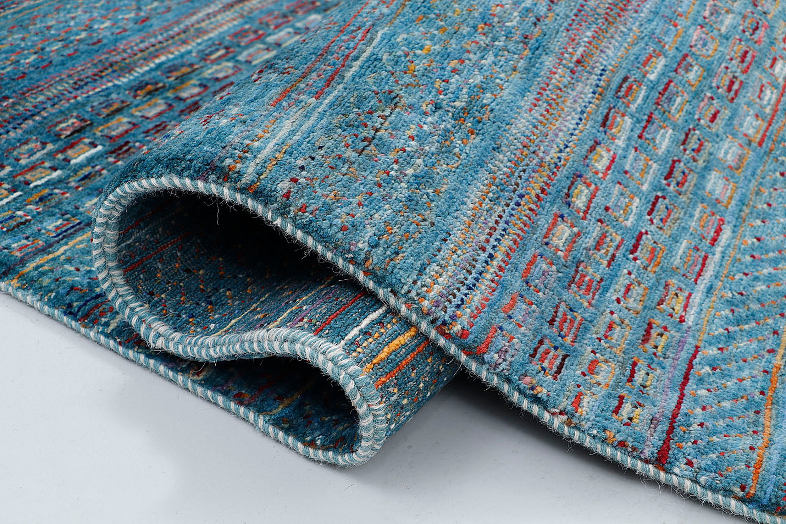 A close-up of a thick-pile wool rug highlighting the dense, plush texture and the intricate, jewel-toned geometric motifs woven into the rich blue base.