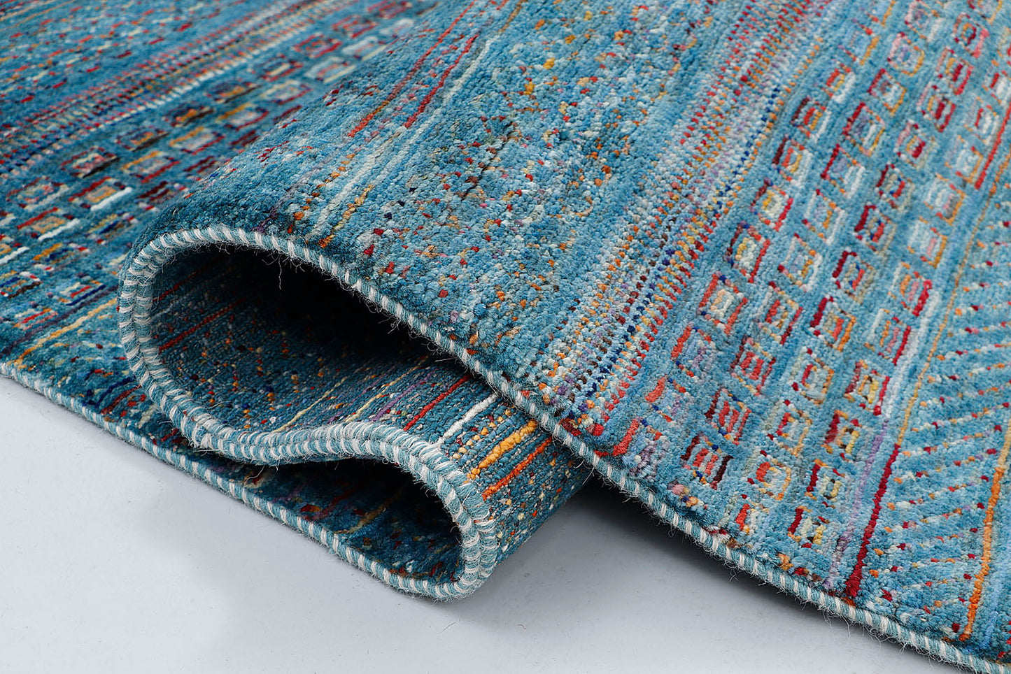 A close-up of a thick-pile wool rug highlighting the dense, plush texture and the intricate, jewel-toned geometric motifs woven into the rich blue base.