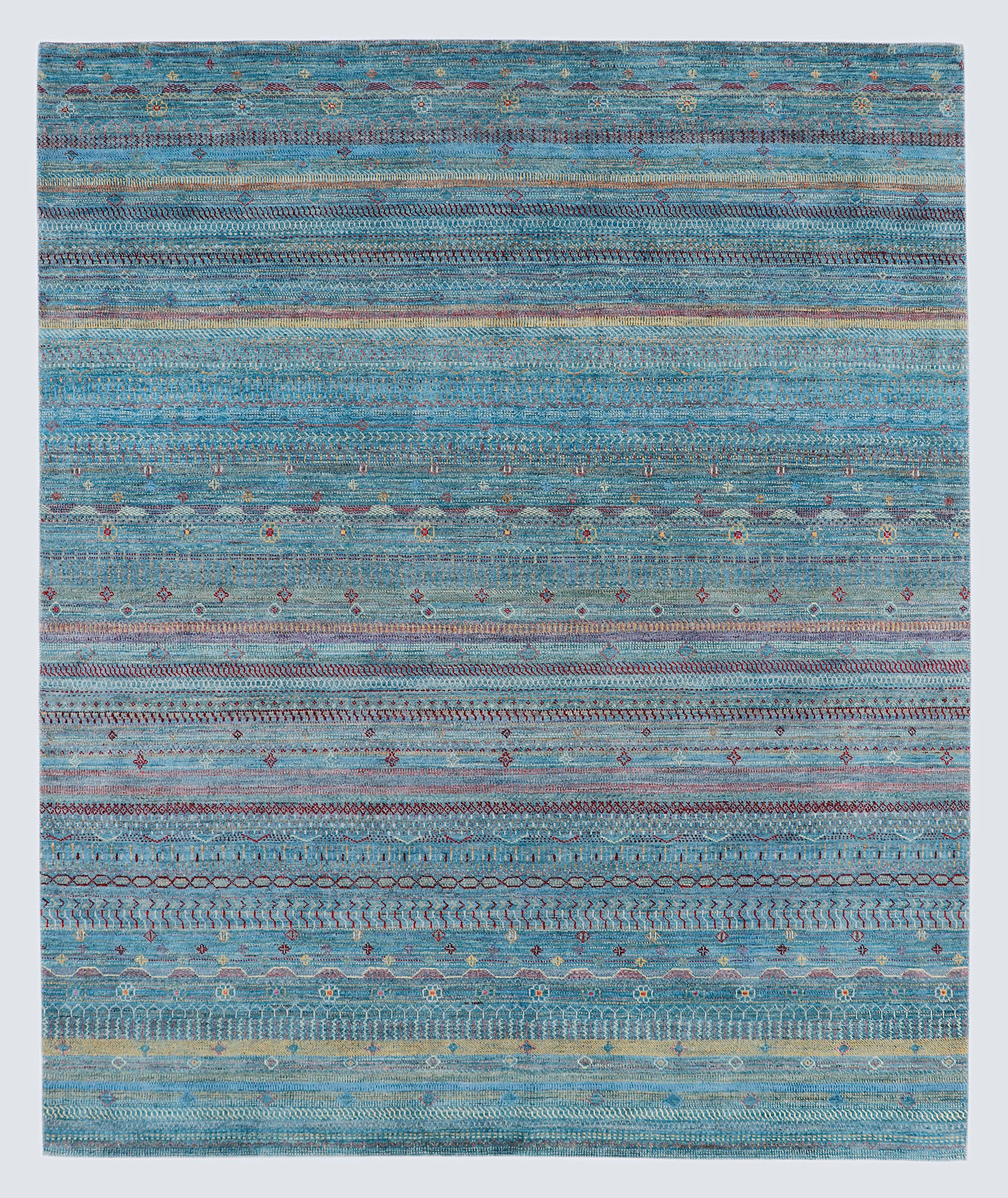A full view of a vibrant hand-knotted Gabbeh rug from the Aatish collection, featuring horizontal bands of saffron and ivory tribal motifs over a striated sea-blue-green foundation.