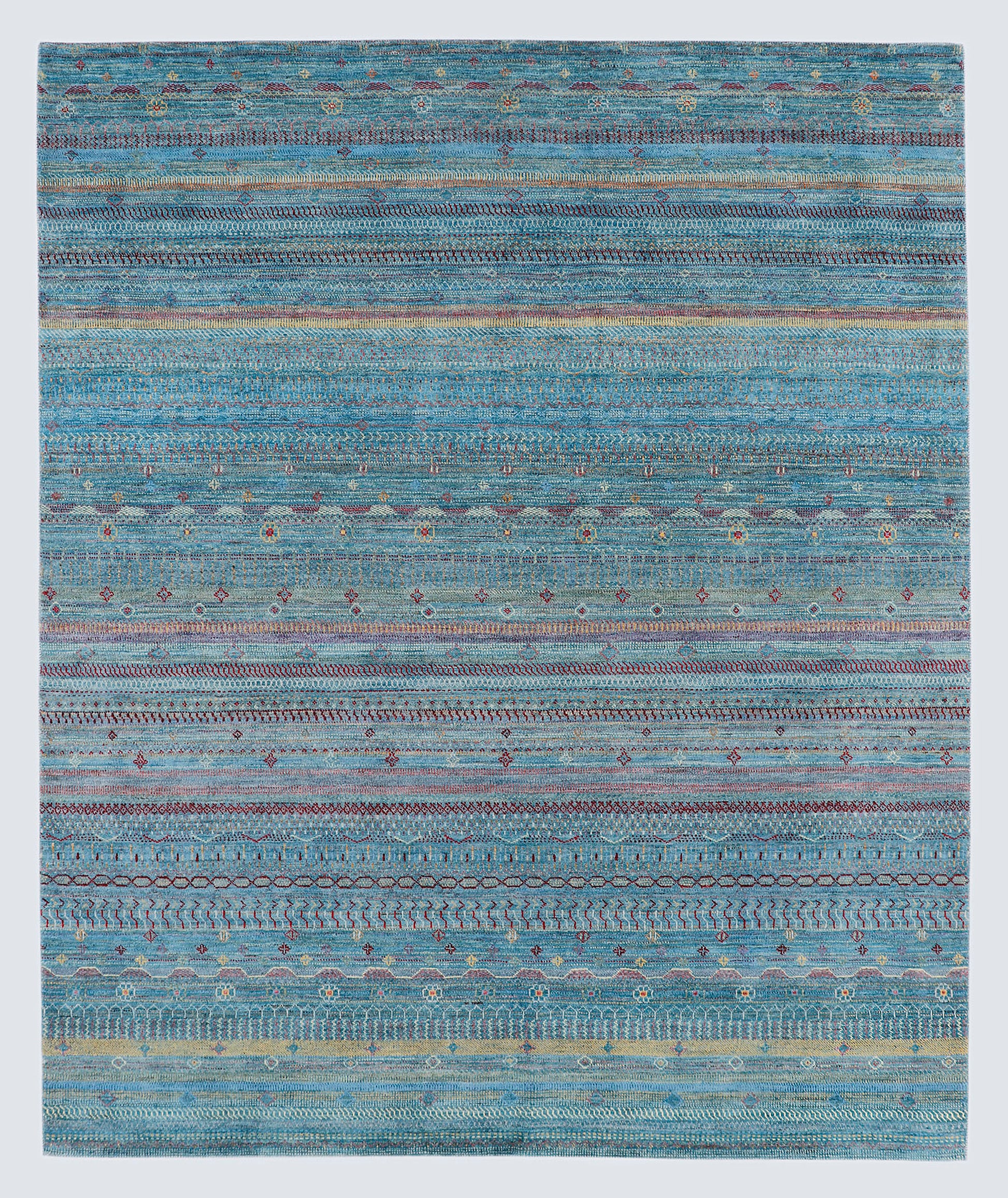 A full view of a vibrant hand-knotted Gabbeh rug from the Aatish collection, featuring horizontal bands of saffron and ivory tribal motifs over a striated sea-blue-green foundation.