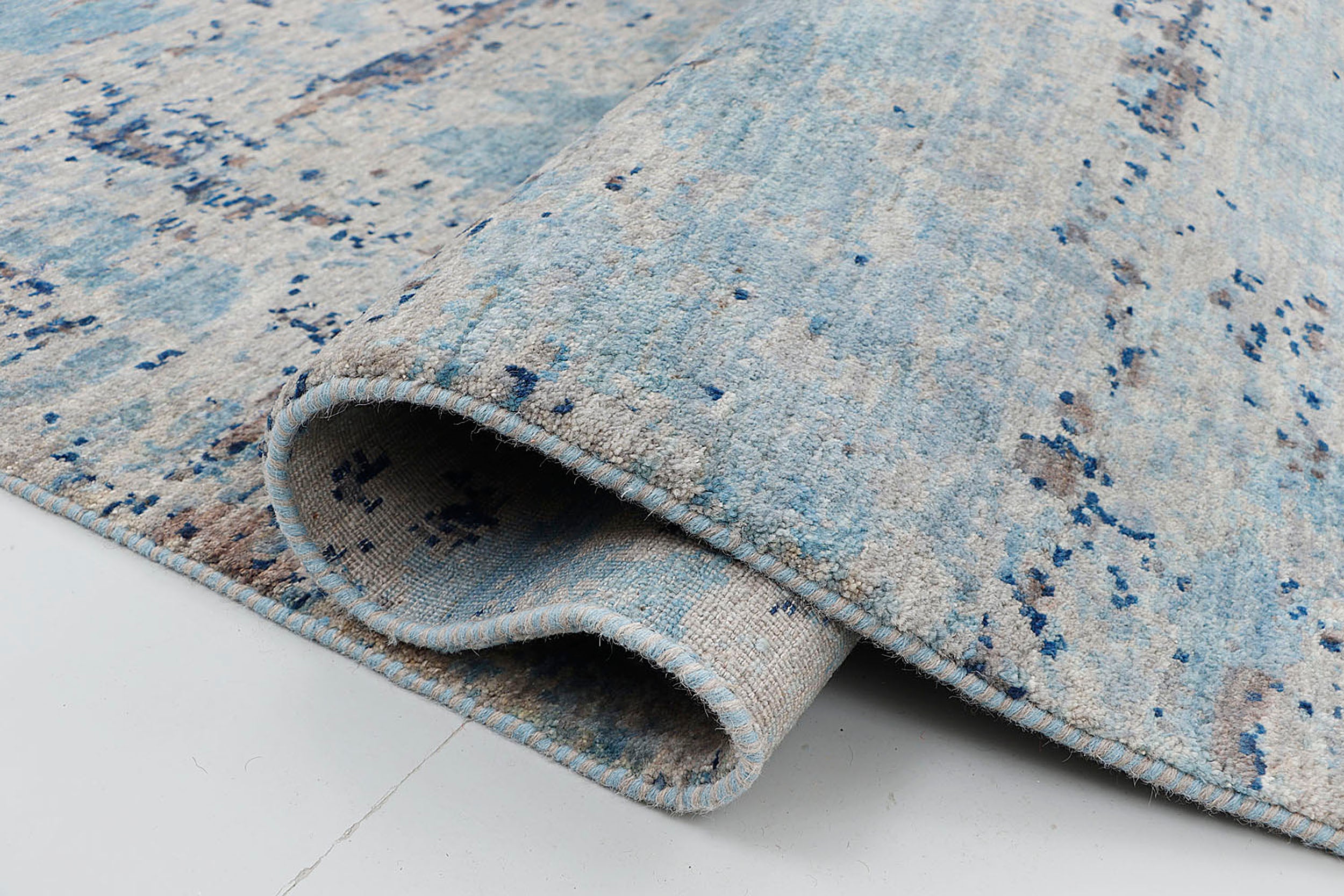 A close-up of a crisp, medium-pile hand-knotted wool rug highlighting the dense, tactile contrast between the cerulean blue and silver-grey yarns in an abstract, scraped-paint effect.