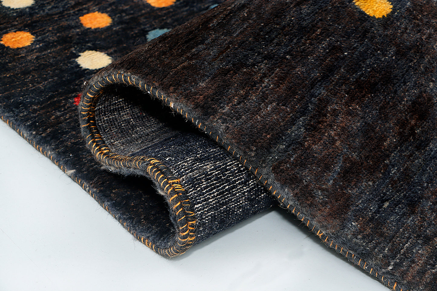A close-up of a pure wool hand-knotted rug highlighting the dense texture of the dark black background contrasting sharply with intricately woven red, yellow, and blue circular motifs.