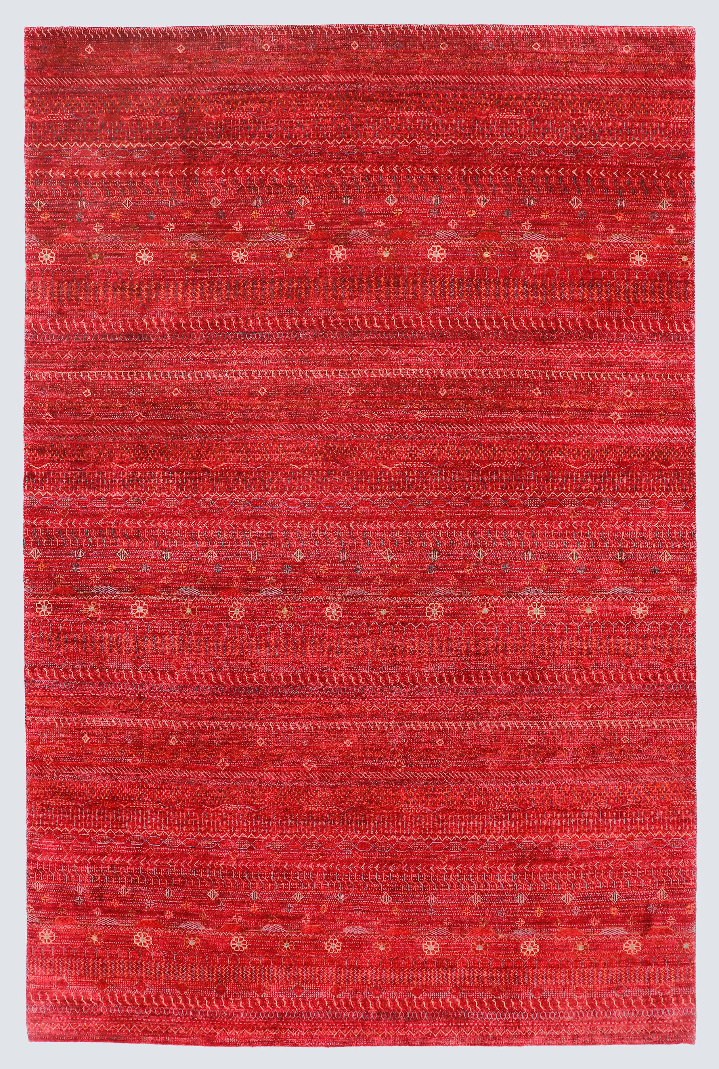 A full view of a vibrant red hand-knotted Gabbeh rug from the Aatish collection, featuring horizontal bands of gold and ivory tribal motifs over a saturated cinnabar foundation.