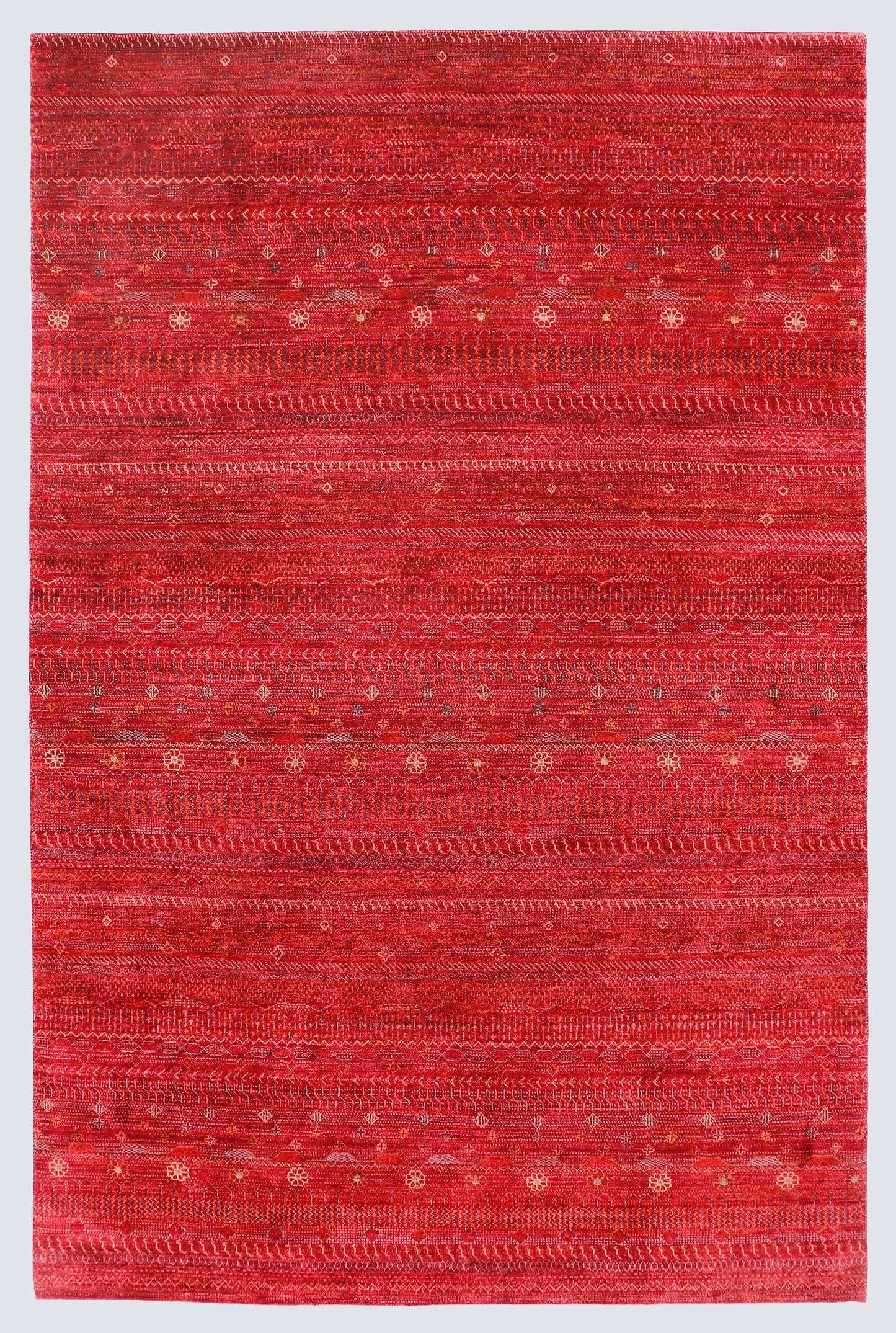 A full view of a vibrant red hand-knotted Gabbeh rug from the Aatish collection, featuring horizontal bands of gold and ivory tribal motifs over a saturated cinnabar foundation.