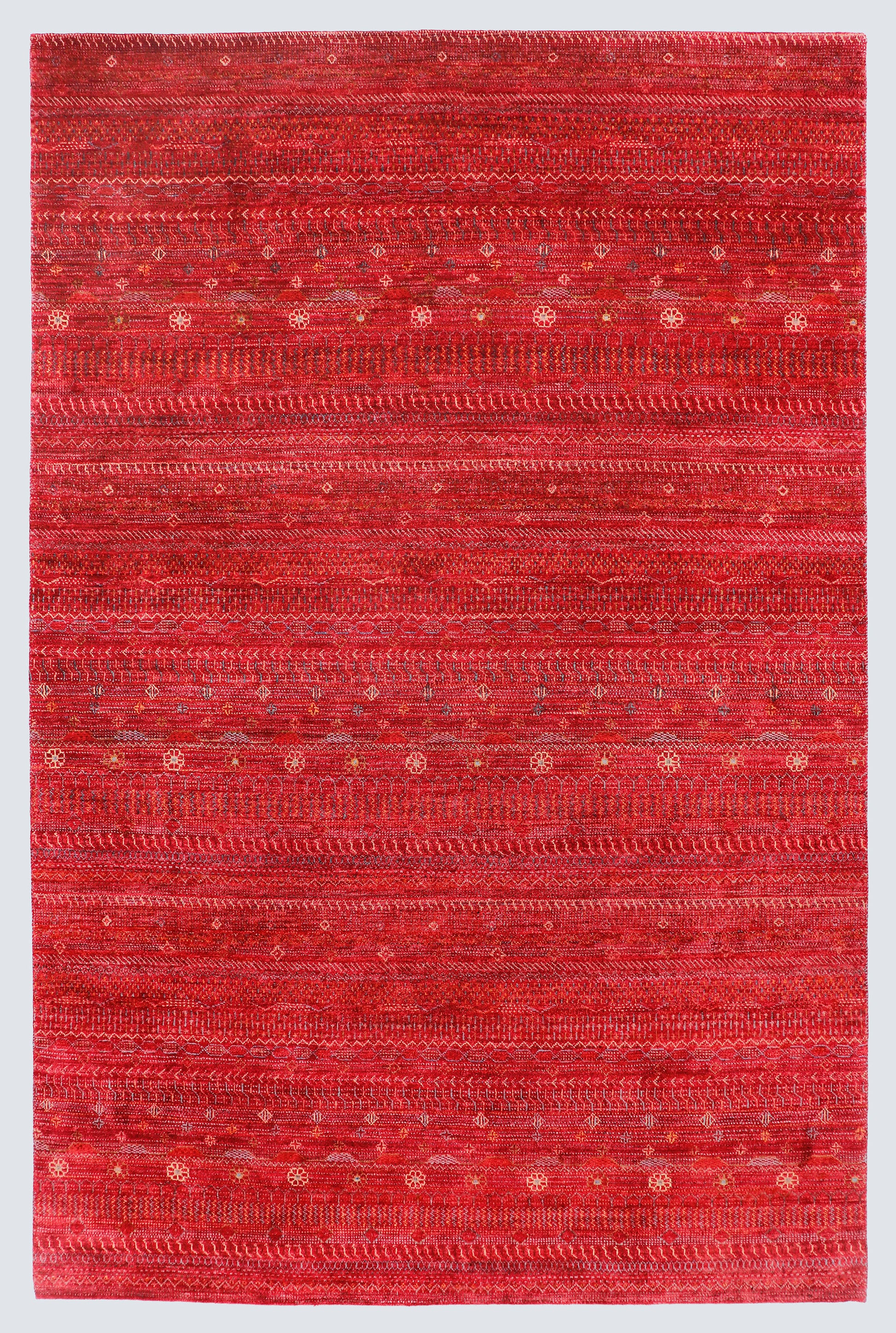A full view of a vibrant red hand-knotted Gabbeh rug from the Aatish collection, featuring horizontal bands of gold and ivory tribal motifs over a saturated cinnabar foundation.