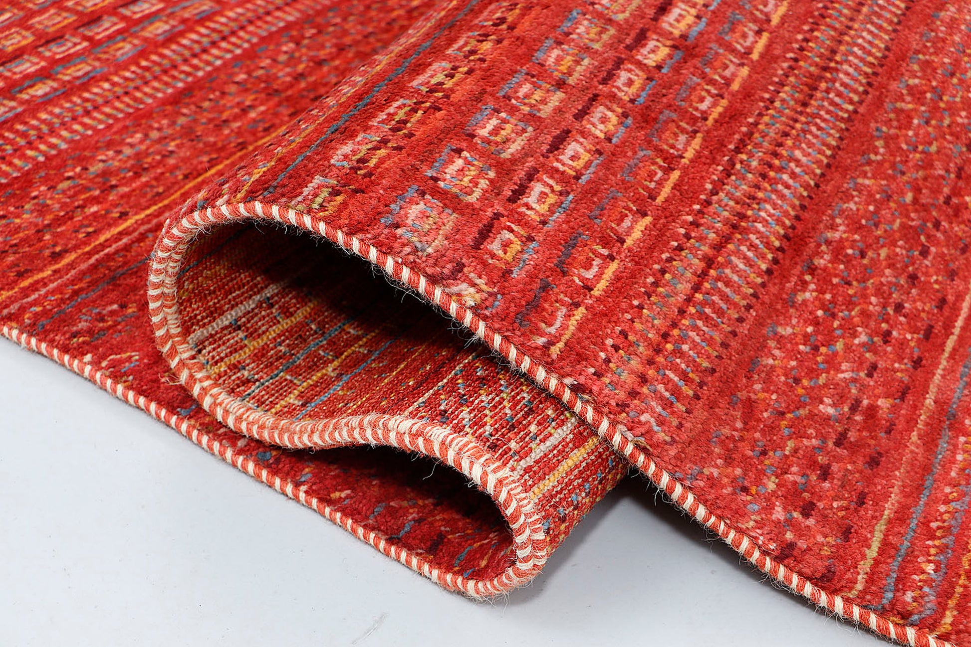 A close-up of a plush wool rug highlighting the dense, hand-knotted texture and the rhythmic, multi-colored geometric symbols woven into the warm, kiln-fired base.