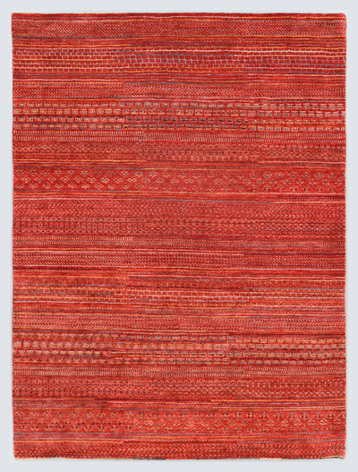 A full view of an earthy, hand-knotted Gabbeh rug from the Aatish collection, featuring horizontal bands of gold and slate blue tribal motifs over a textured copper-rust foundation.