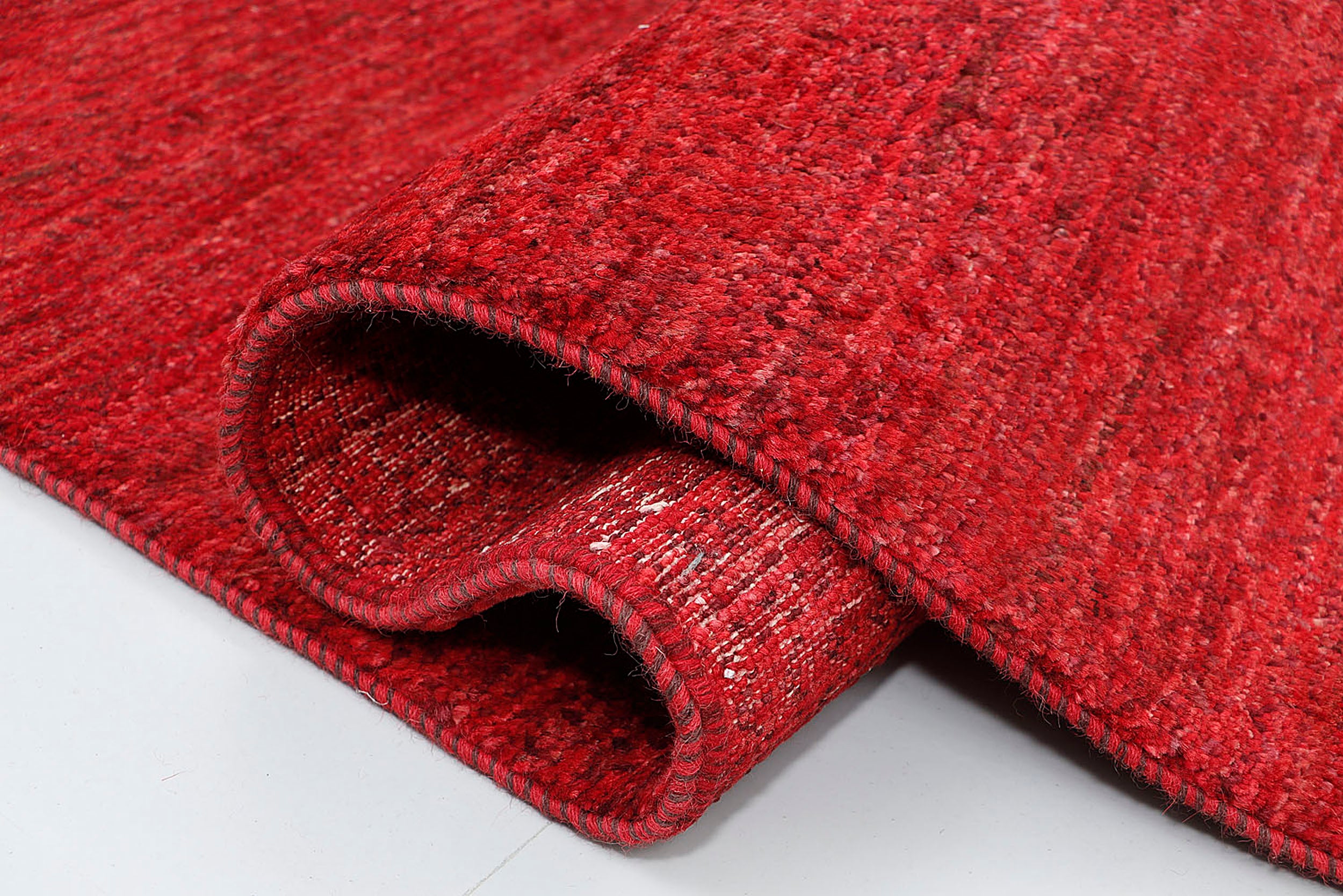 A close-up of a plush, thick-pile hand-knotted wool rug highlighting the organic, horizontal color shifts and dense, comforting texture of the solid red yarn.