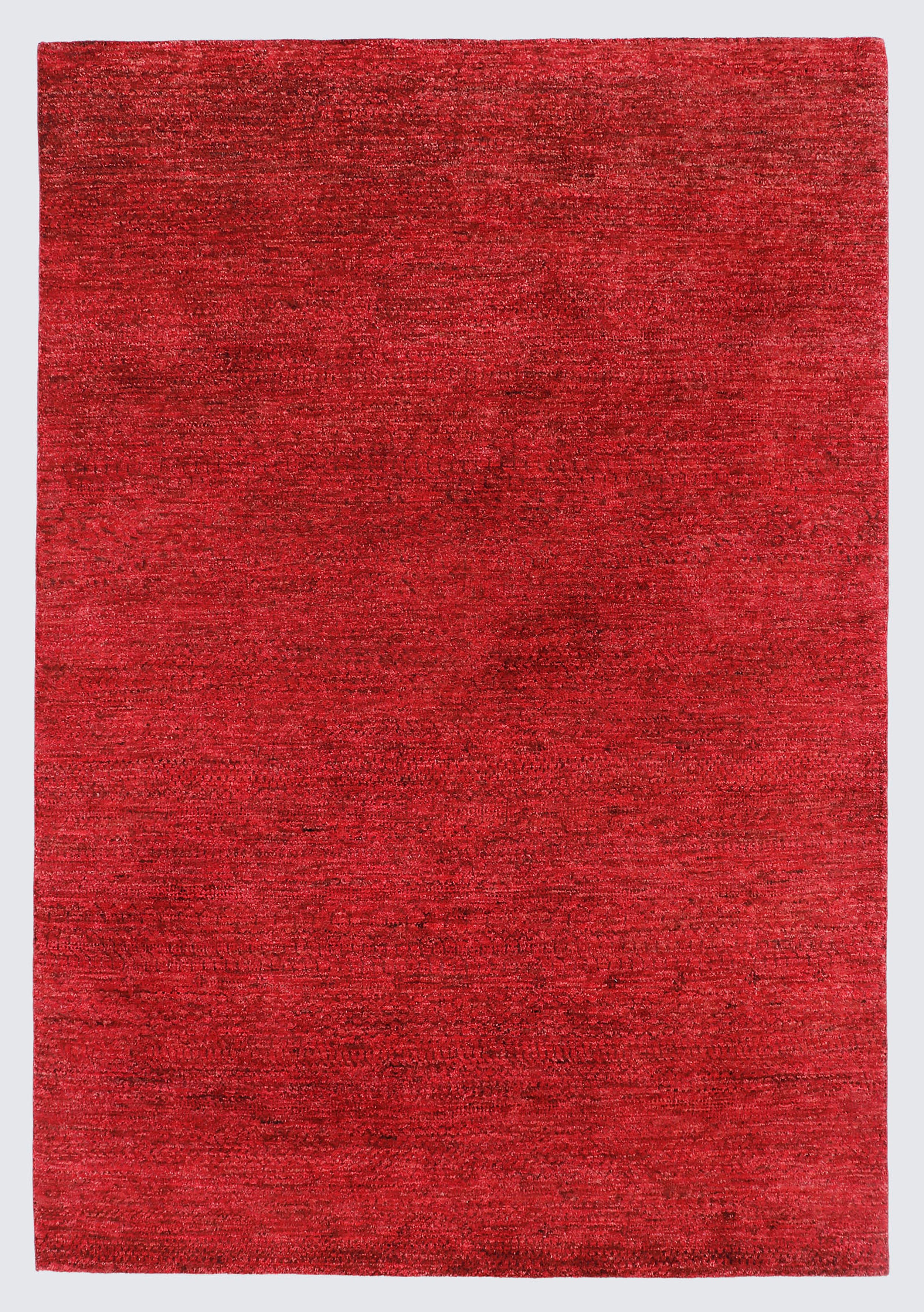 A full view of a minimalist hand-knotted Gabbeh rug from the Aatish collection, featuring a solid, heavily textured field of rich crimson and ruby red.