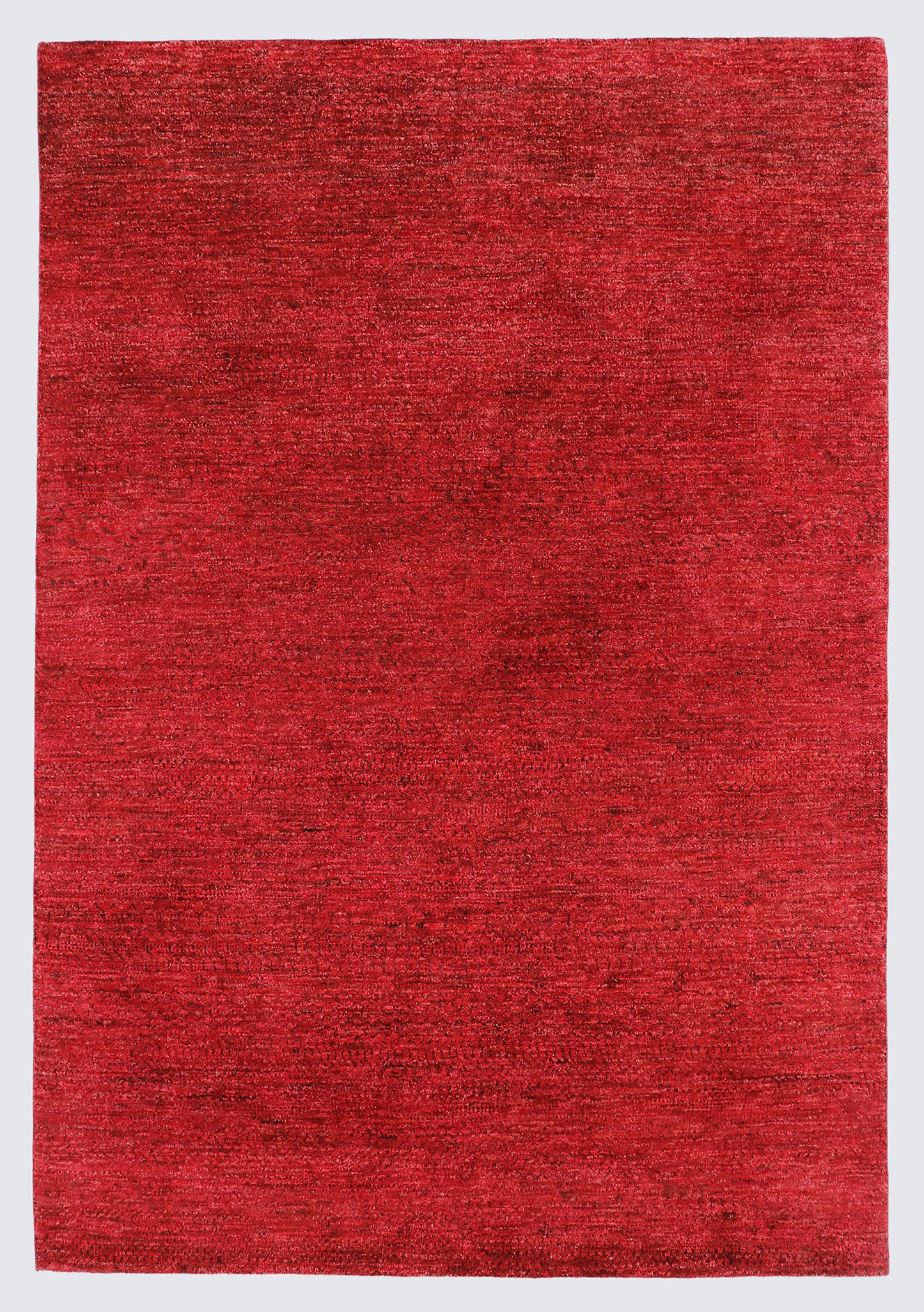 A full view of a minimalist hand-knotted Gabbeh rug from the Aatish collection, featuring a solid, heavily textured field of rich crimson and ruby red.
