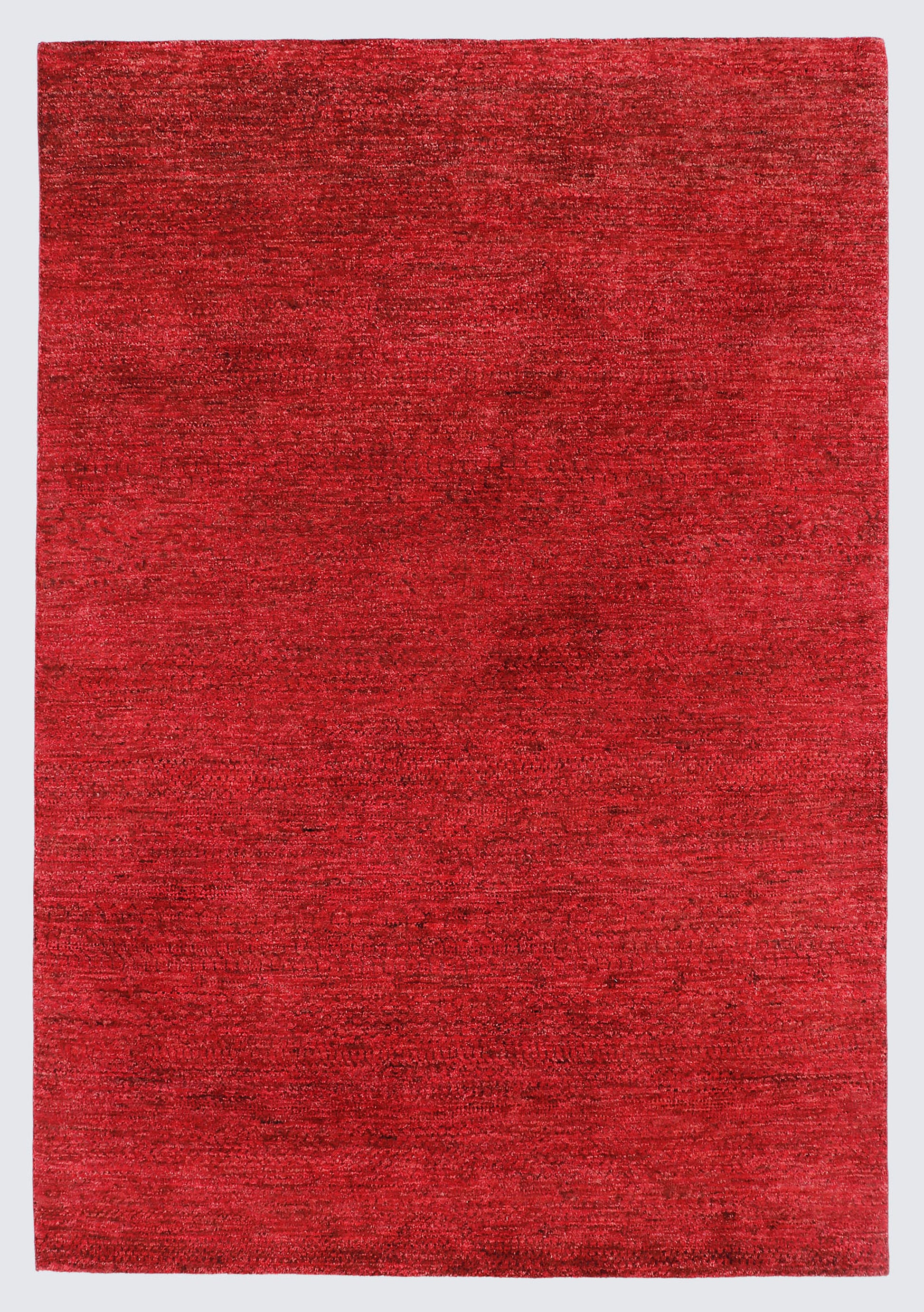 A full view of a minimalist hand-knotted Gabbeh rug from the Aatish collection, featuring a solid, heavily textured field of rich crimson and ruby red.