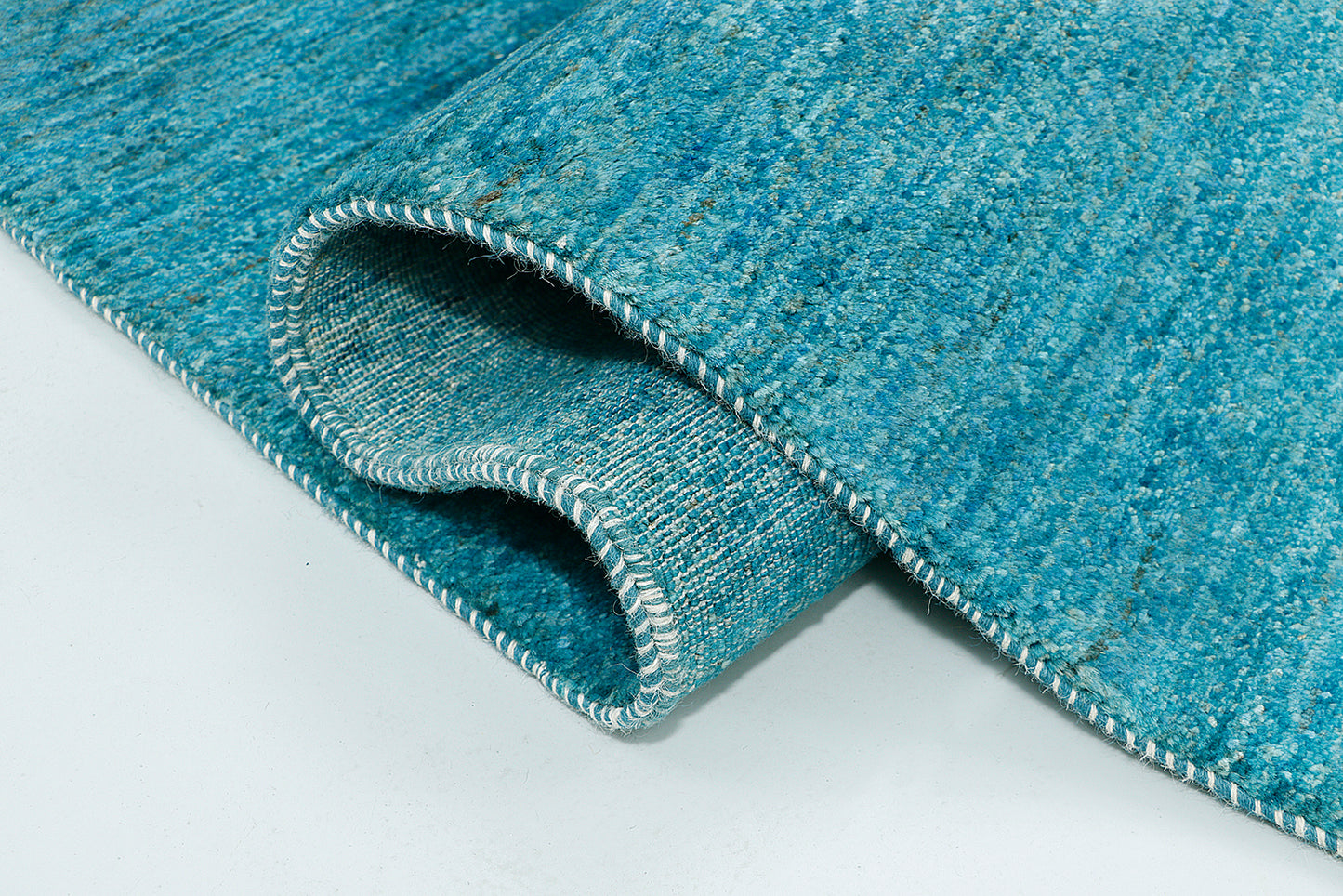 A high-resolution close-up of a cyan wool rug highlighting the double-knot construction and the natural color variance created by hand-spun, AZO-free dyes.