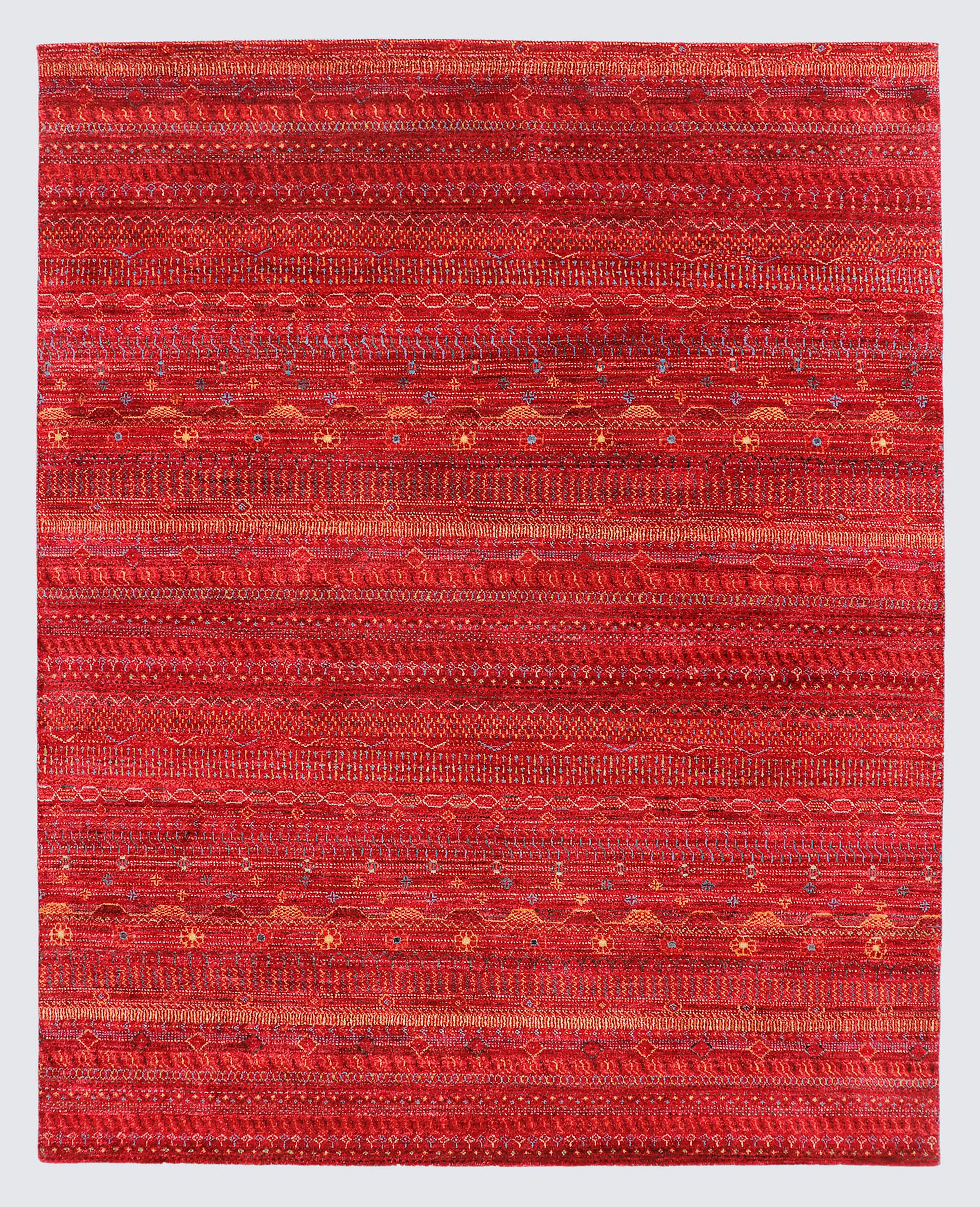 A full view of an earthy, hand-knotted Gabbeh rug from the Aatish collection, featuring horizontal bands of gold, orange, and teal tribal motifs over a textured rust-red foundation.