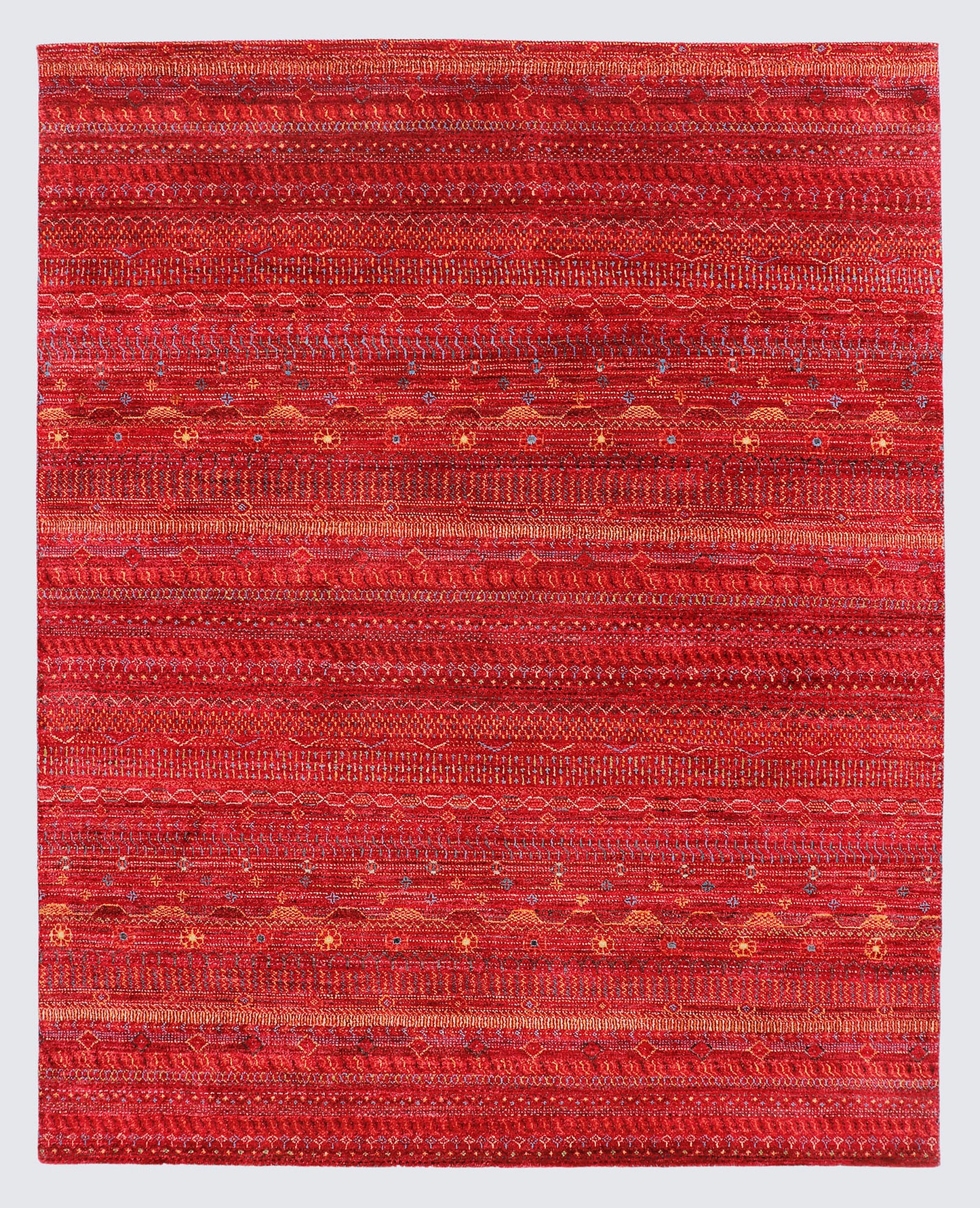 A full view of an earthy, hand-knotted Gabbeh rug from the Aatish collection, featuring horizontal bands of gold, orange, and teal tribal motifs over a textured rust-red foundation.