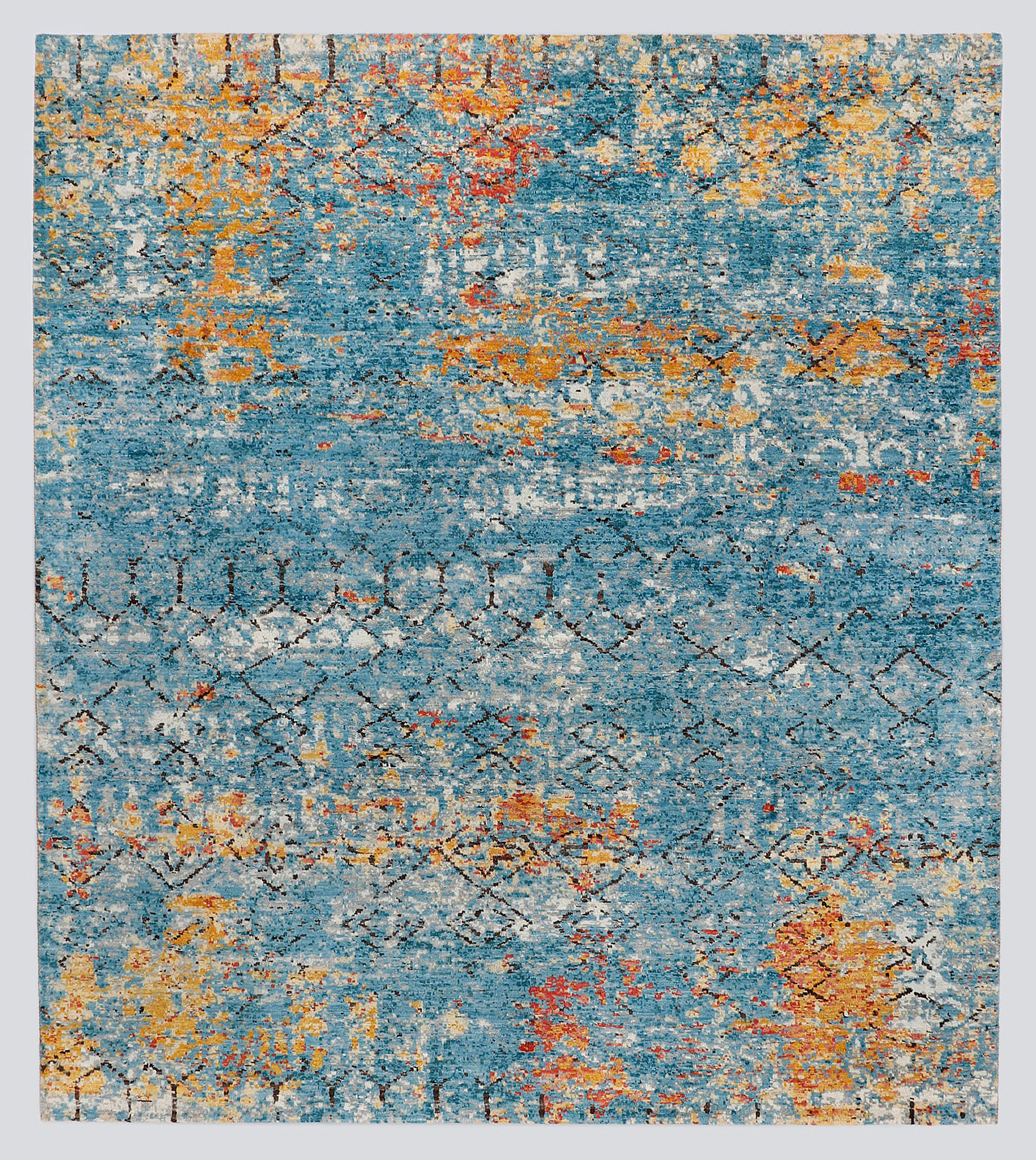 A full view of a modern transitional hand-knotted rug featuring a heavily distressed wash of lapis blue and fiery copper obscuring a classic nomadic geometric pattern.