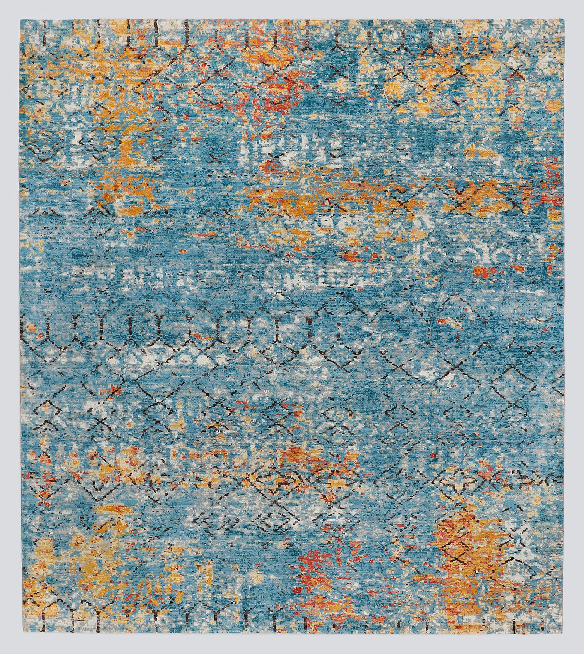 A full view of a modern transitional hand-knotted rug featuring a heavily distressed wash of lapis blue and fiery copper obscuring a classic nomadic geometric pattern.