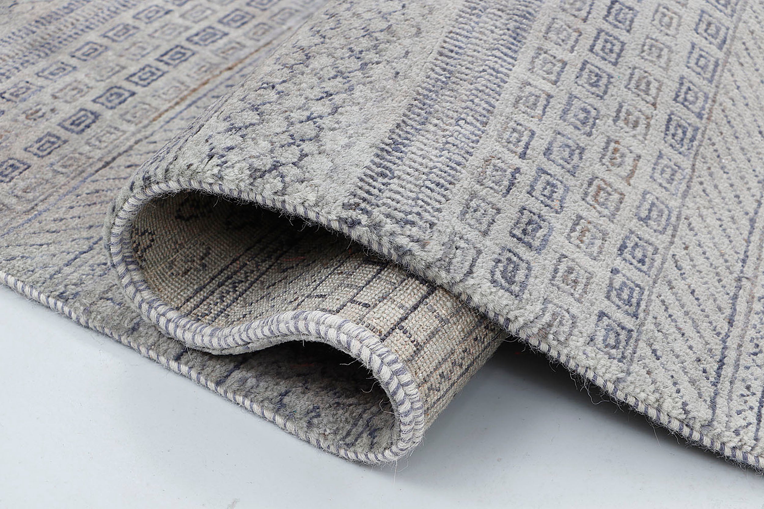 A close-up of a thick-pile hand-knotted wool rug highlighting the dense texture and the rhythmic, "script-like" rows of dark grey nomadic motifs.