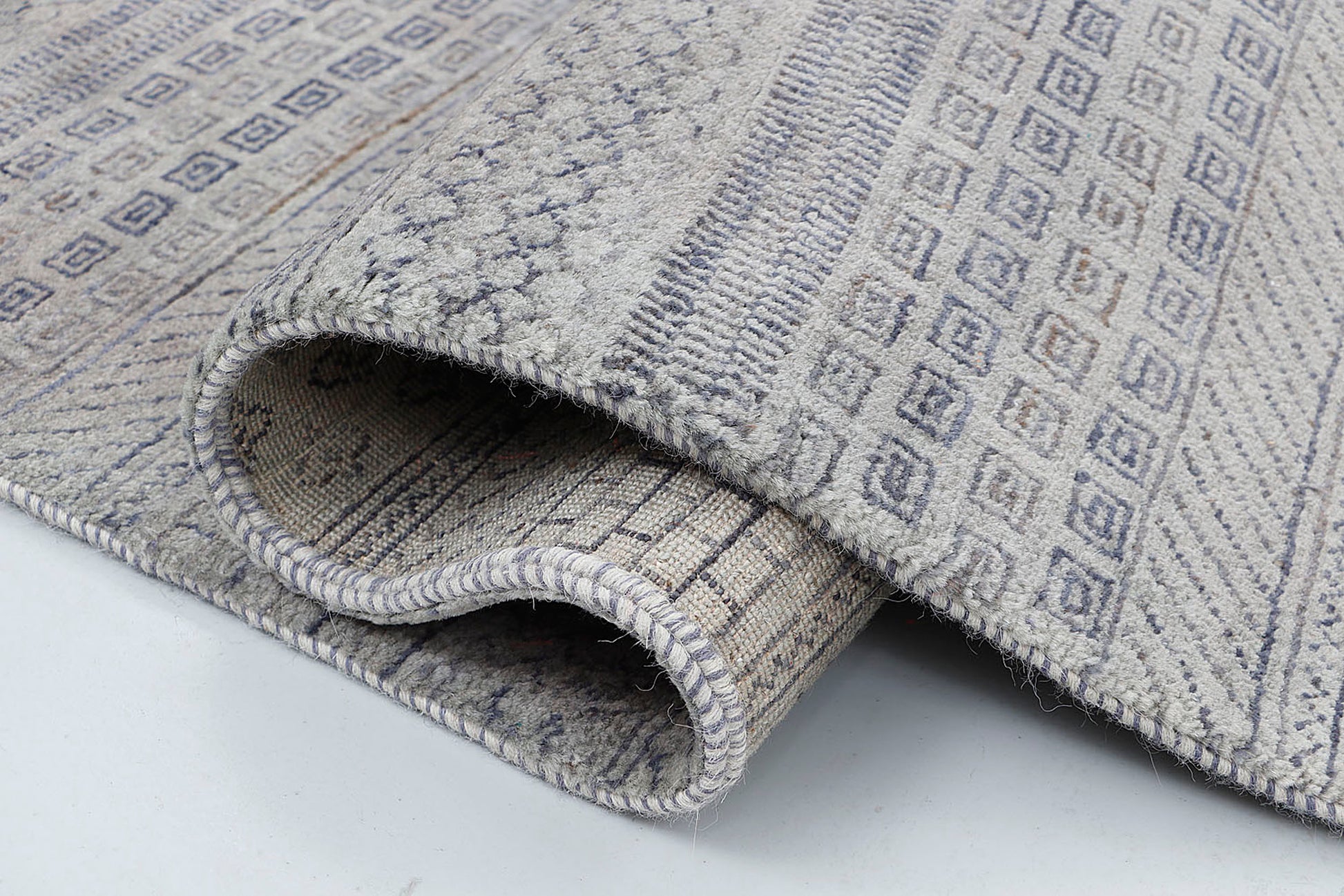 A close-up of a thick-pile hand-knotted wool rug highlighting the dense texture and the rhythmic, "script-like" rows of dark grey nomadic motifs.