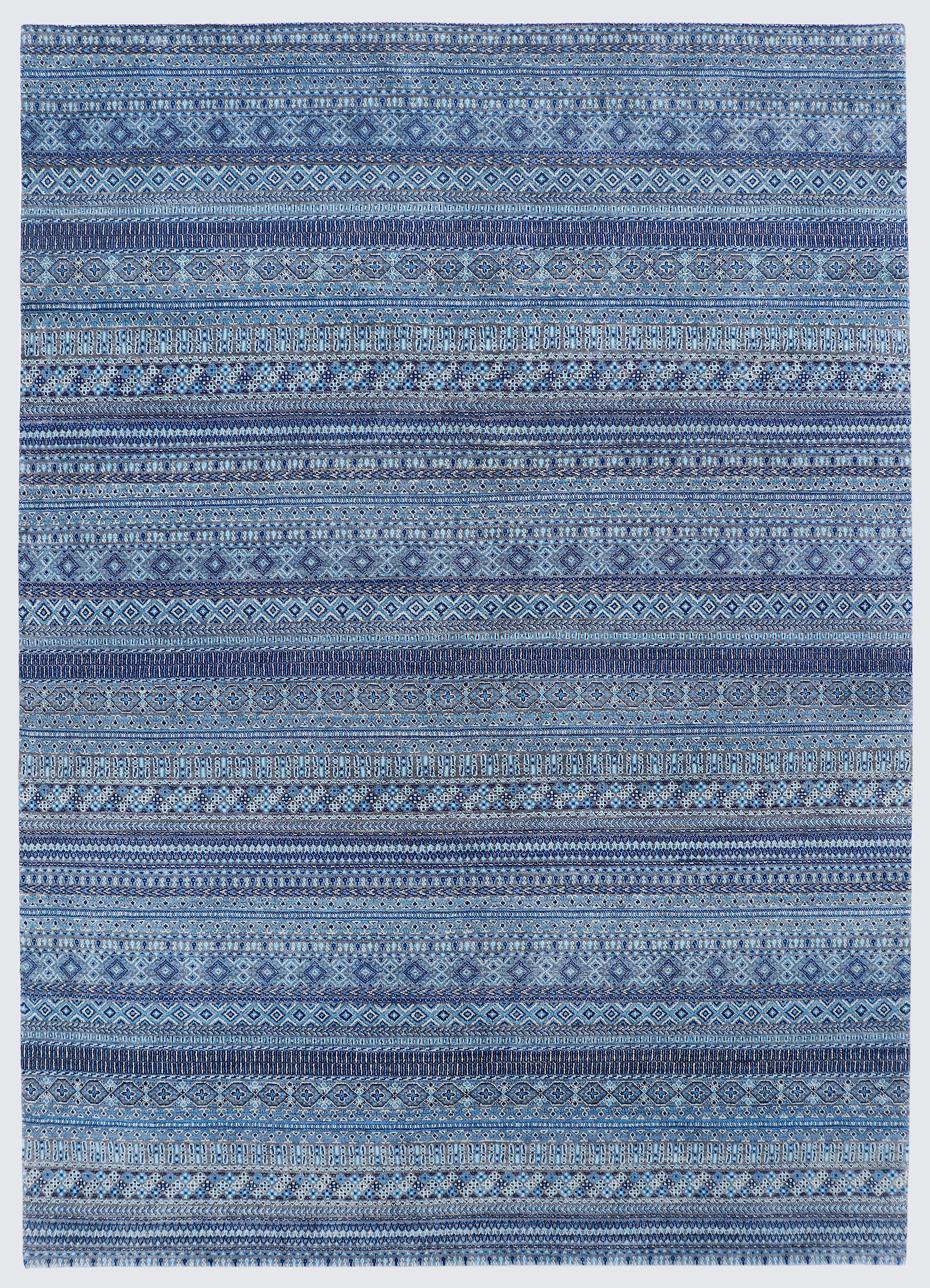 A full view of a hand-knotted wool rug featuring dense horizontal bands of miniature tribal motifs in a calming monochromatic palette of indigo, steel blue, and soft azure.