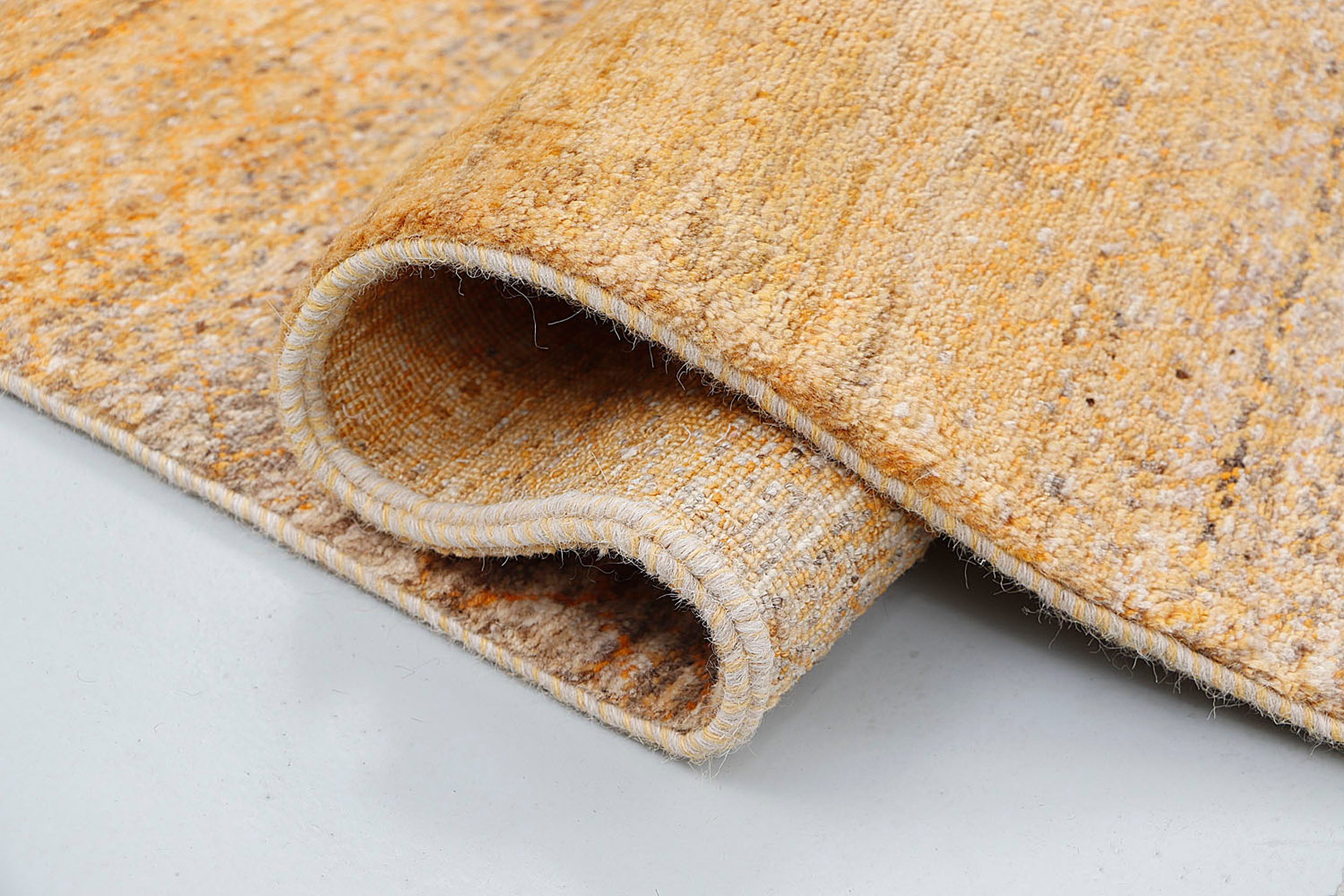A close-up of a crisp, medium-pile wool rug highlighting subtle, tone-on-tone woven textures and faint geometric patterns within a golden ochre base.