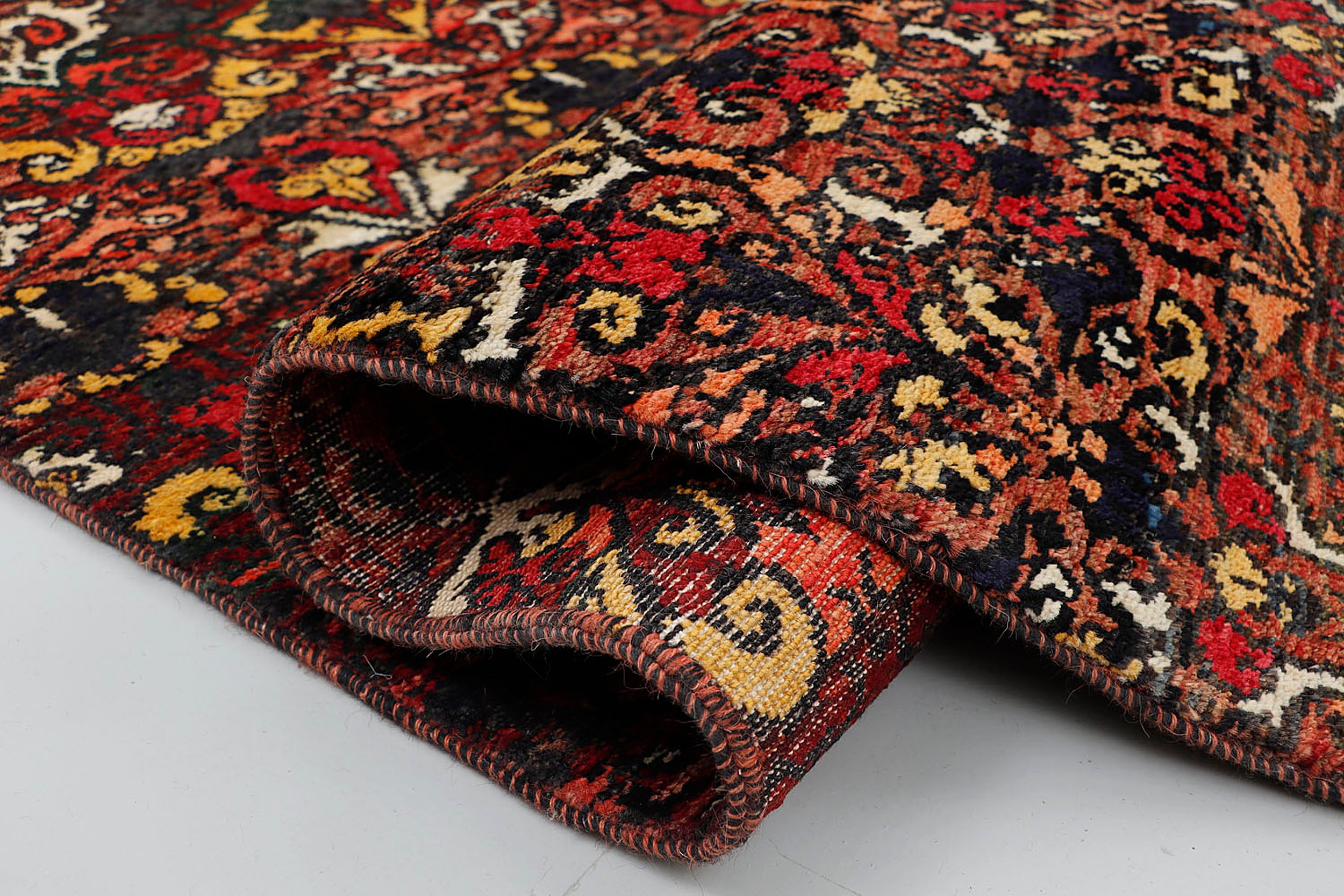 A close-up of a dense, hand-knotted wool rug highlighting the intense color contrast and rich tactile depth between the glowing jewel-toned patterns and the dark background.