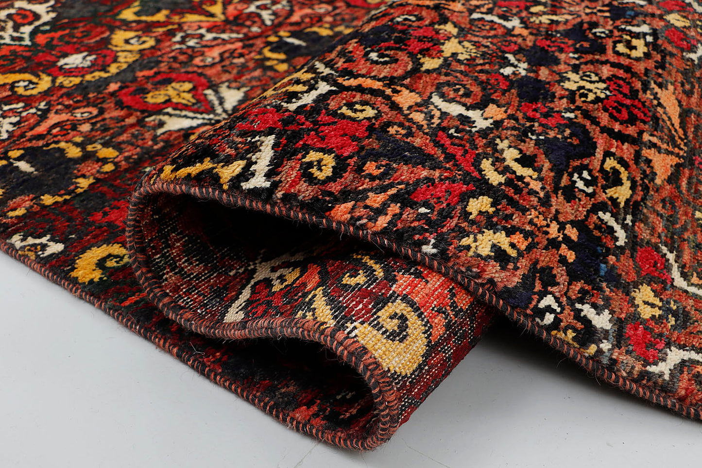 A close-up of a dense, hand-knotted wool rug highlighting the intense color contrast and rich tactile depth between the glowing jewel-toned patterns and the dark background.