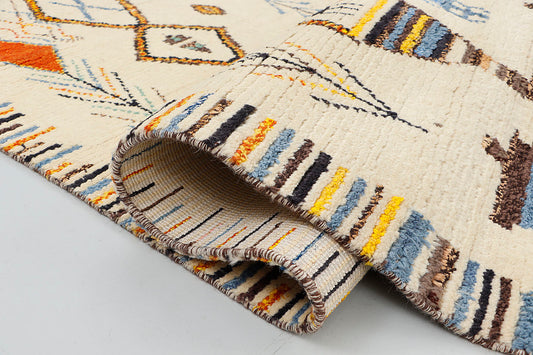 A close-up highlighting the plush, thick wool pile of a cream rug, detailing the intricate knotting of indigo blue and burnt orange tribal symbols and the textured edge of a colorful striped border.