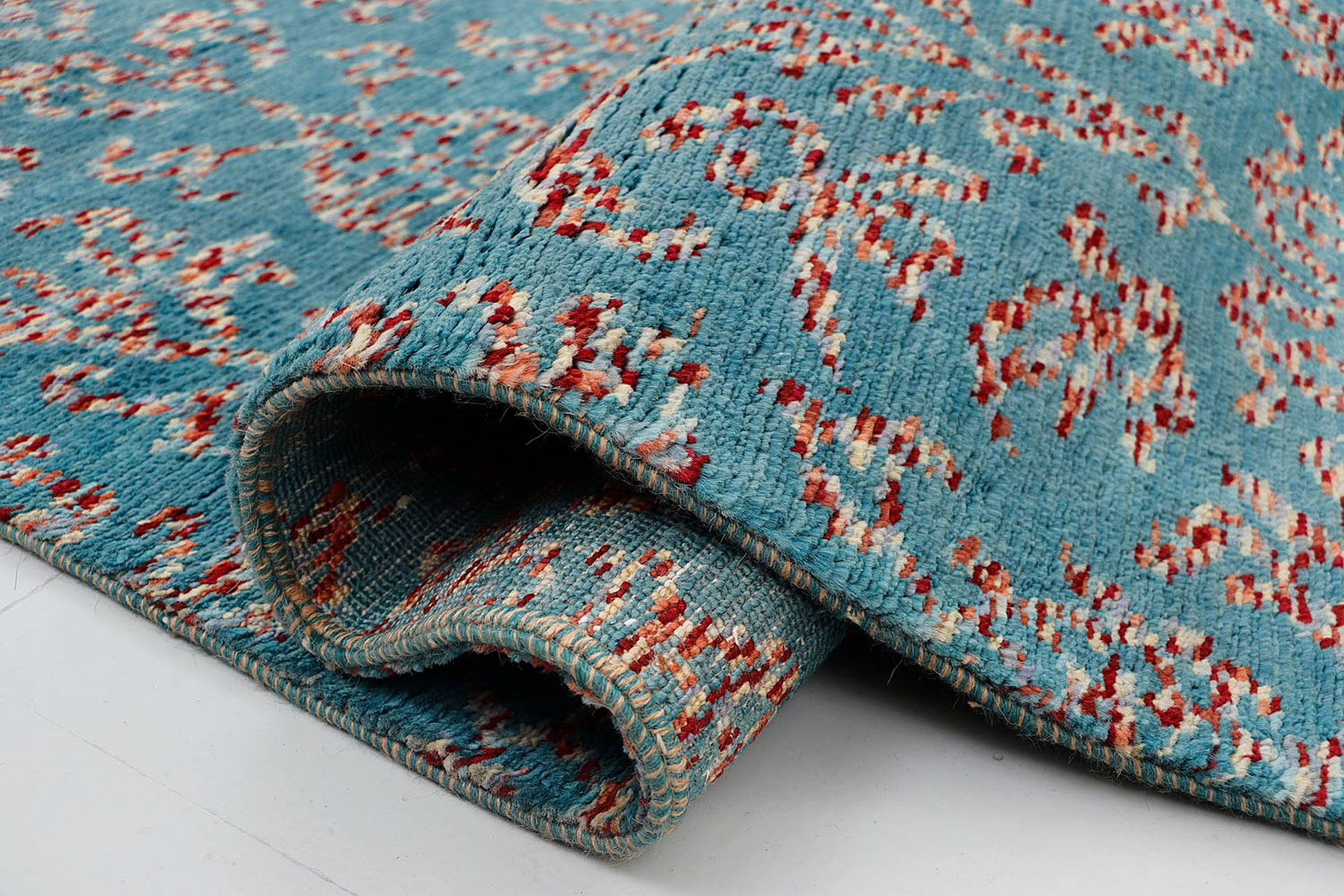 A close-up of a crisp, uniform-pile hand-knotted wool rug highlighting the complex artisan technique of using shifting, multi-colored tie-dyed yarns to form traditional repeating motifs against a bright blue background.