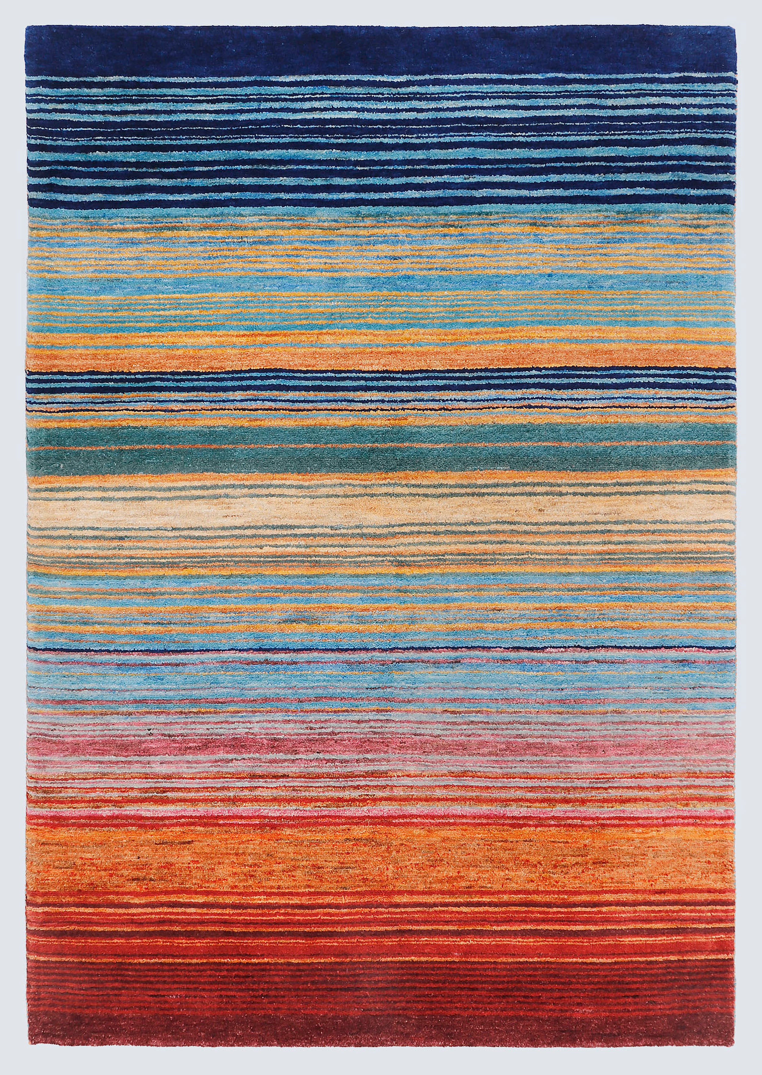 A full view of a vibrant hand-knotted Gabbeh rug from the Aatish collection, featuring horizontal stripes in a full color spectrum from deep indigo and teal to orange and rich terracotta.