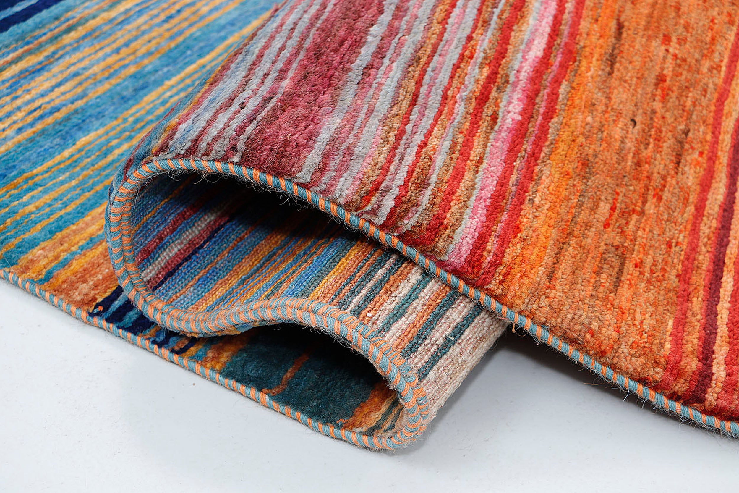 A close-up of a thick-pile wool rug highlighting the dense, matte texture and the smooth transition between saturated horizontal color bands.