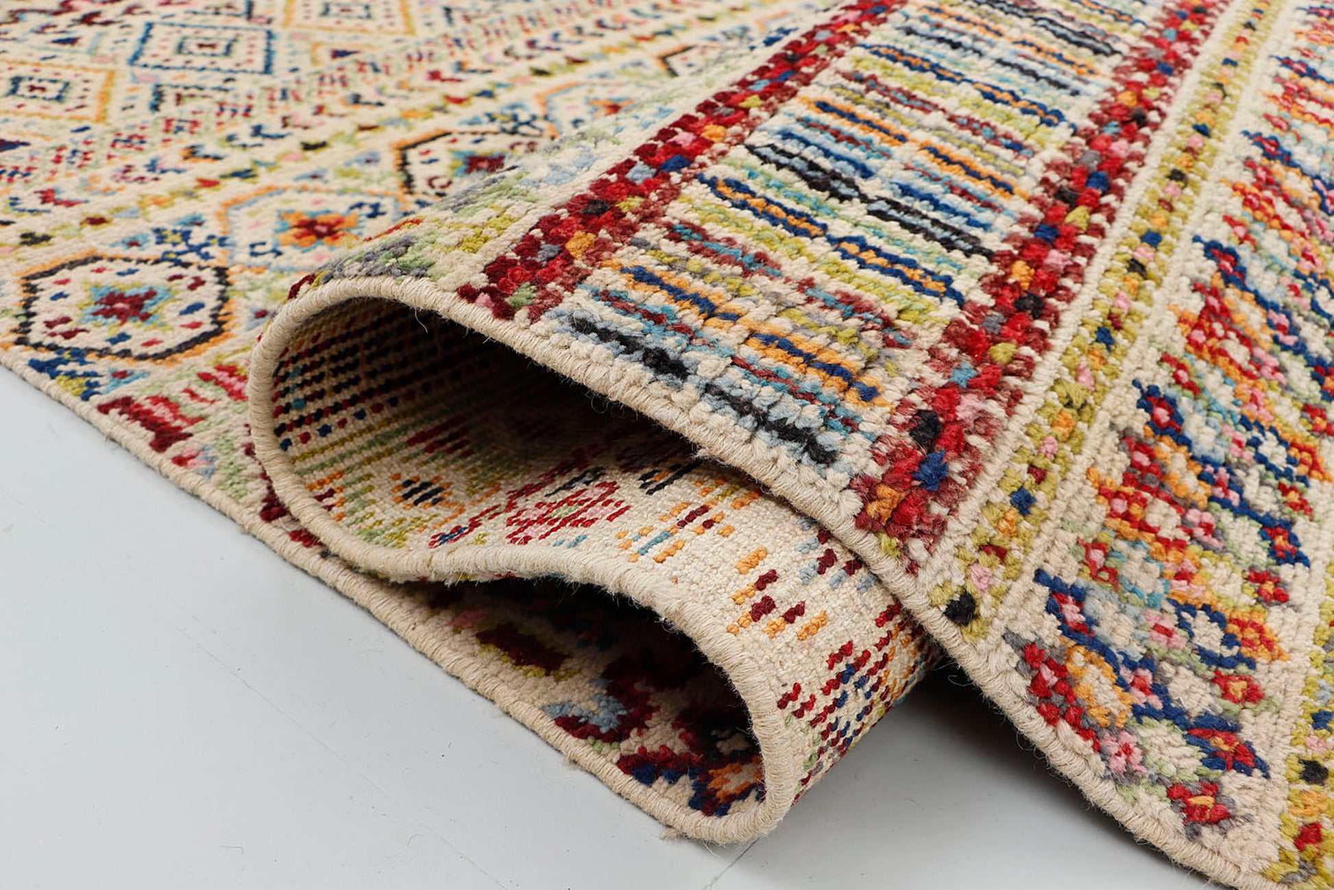A close-up of a brightly colored, medium-pile wool rug showcasing crisp, Persian double-knotted geometric diamonds and traditional latch-hook patterns.