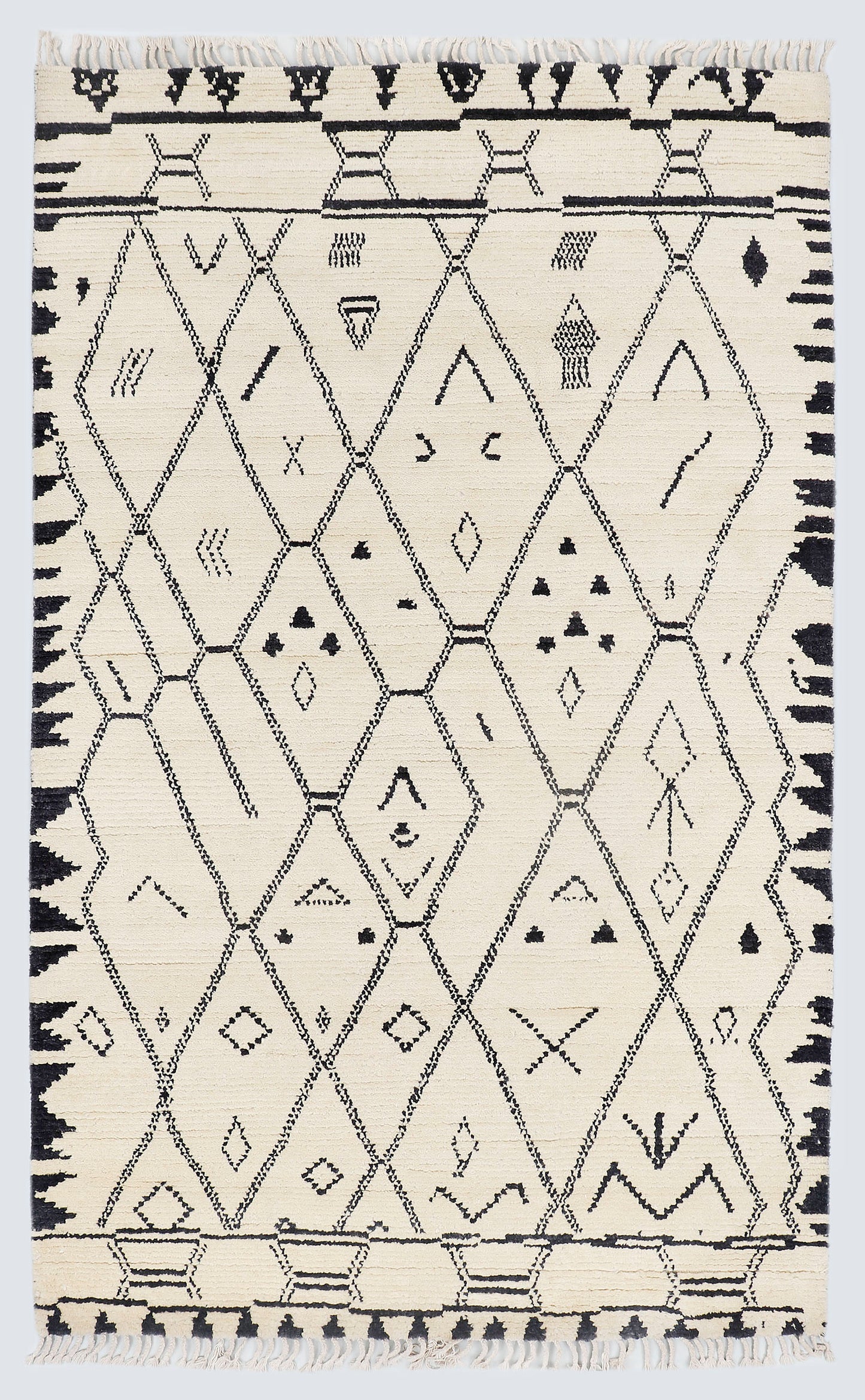 A full view of a hand-knotted, high-pile Moroccan style rug featuring a natural cream background with a large charcoal black diamond lattice pattern, scattered tribal motifs, and thick, jagged charcoal borders