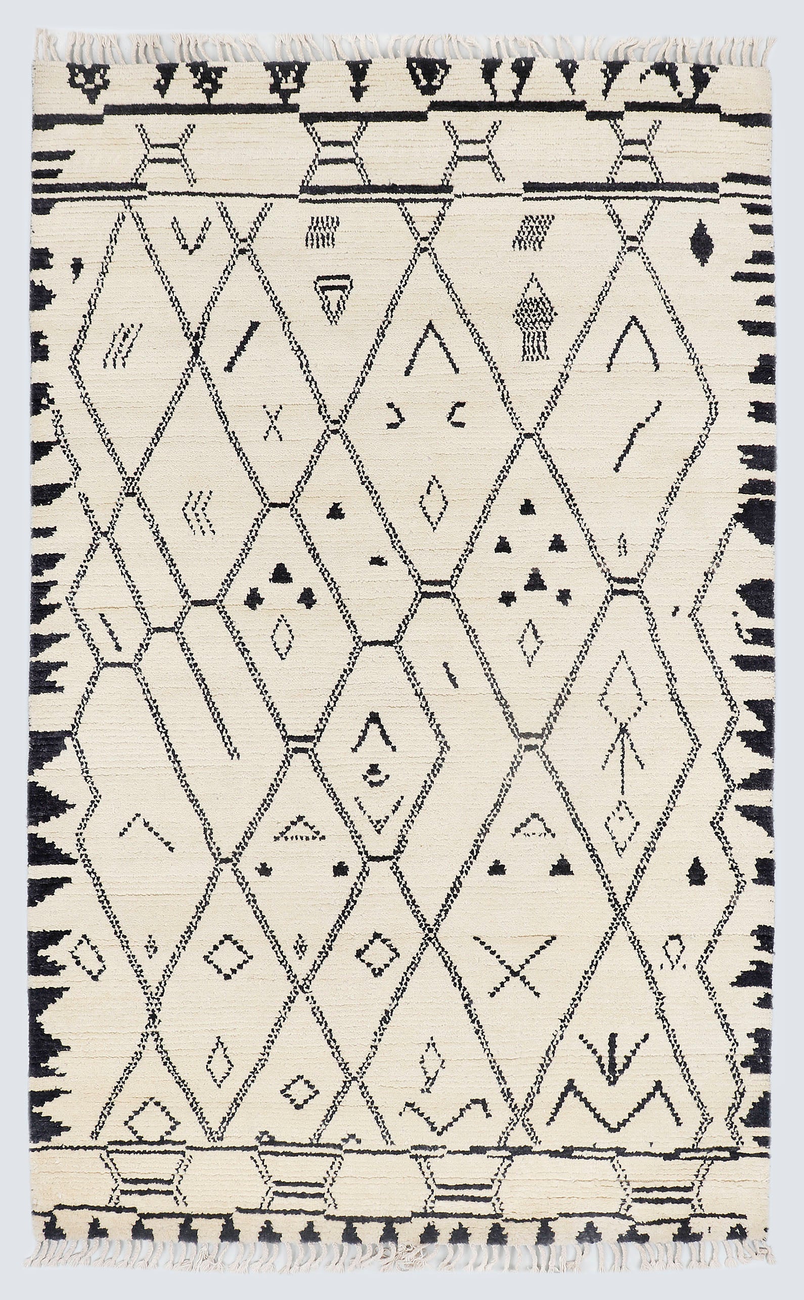 A full view of a hand-knotted, high-pile Moroccan style rug featuring a natural cream background with a large charcoal black diamond lattice pattern, scattered tribal motifs, and thick, jagged charcoal borders