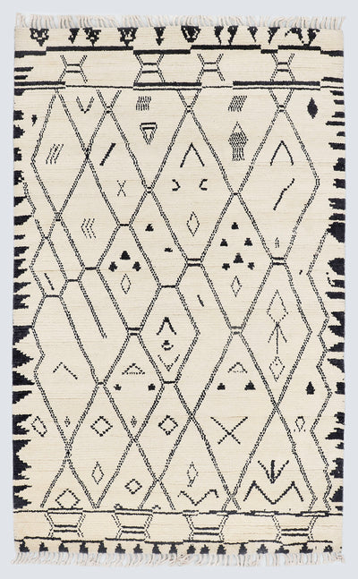 A full view of a hand-knotted, high-pile Moroccan style rug featuring a natural cream background with a large charcoal black diamond lattice pattern, scattered tribal motifs, and thick, jagged charcoal borders