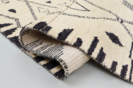 A close-up view highlighting the plush, thick texture of a cream wool rug, showing the intricate hand-knotted charcoal black lines of a traditional tribal diamond pattern.