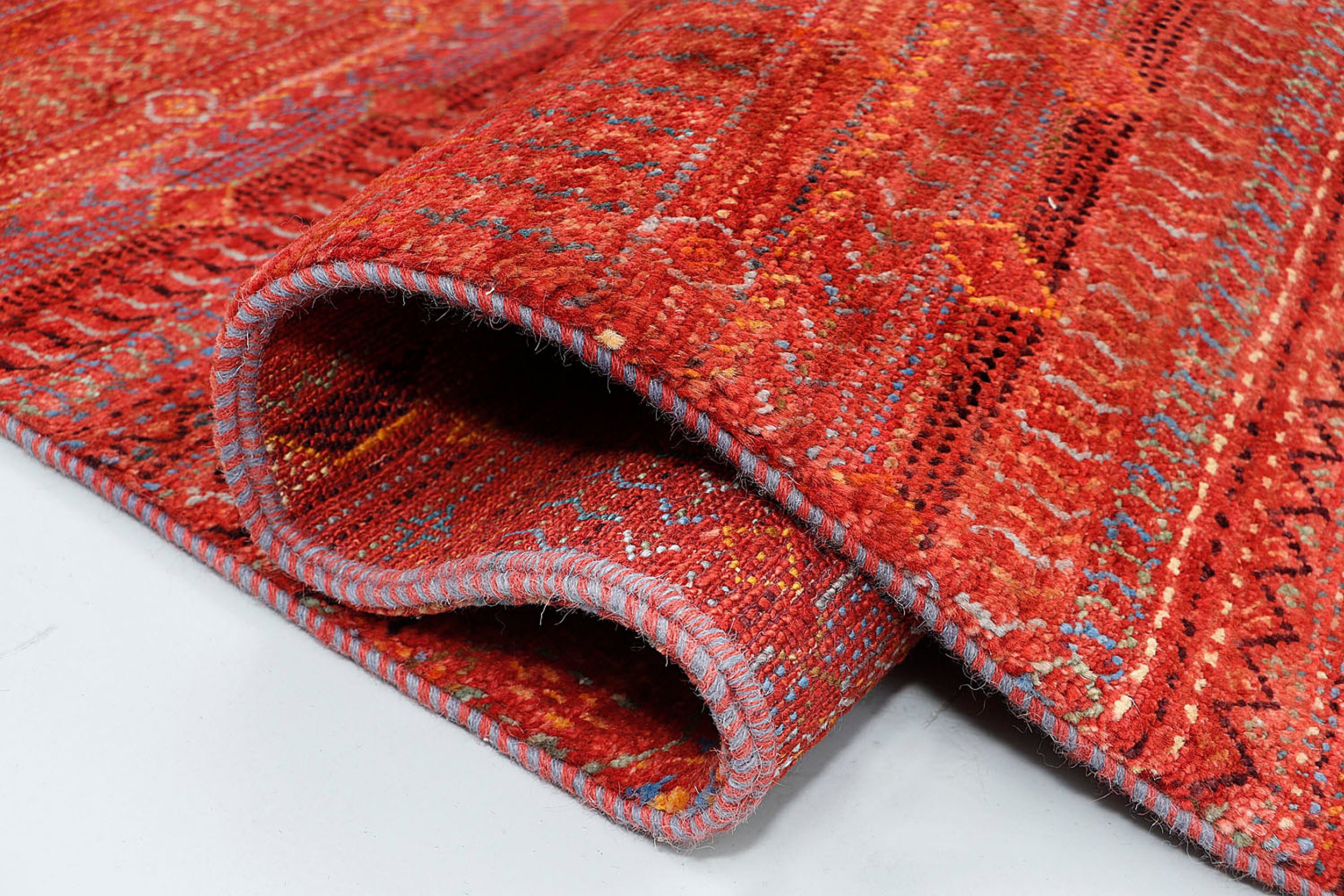 A high-resolution close-up highlighting the dense double-knot wool texture and the variegated ombré effect within the intricate red and orange nomadic symbols.