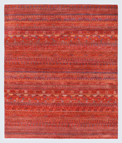 A full view of a warm, hand-knotted Gabbeh rug from the Aatish collection, featuring horizontal bands of gold, blue, white, and green tribal motifs over a heavily textured rust-orange foundation.