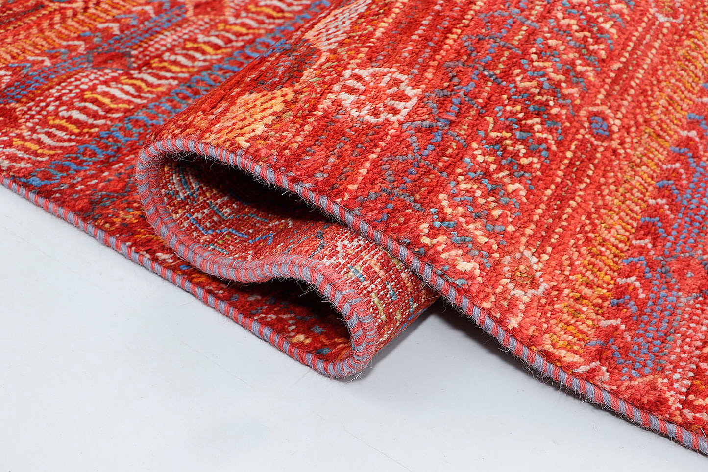 A close-up of a thick-pile wool rug highlighting the plush, organic texture and the vibrant, multi-colored geometric motifs woven into the earthy russet-red base.
