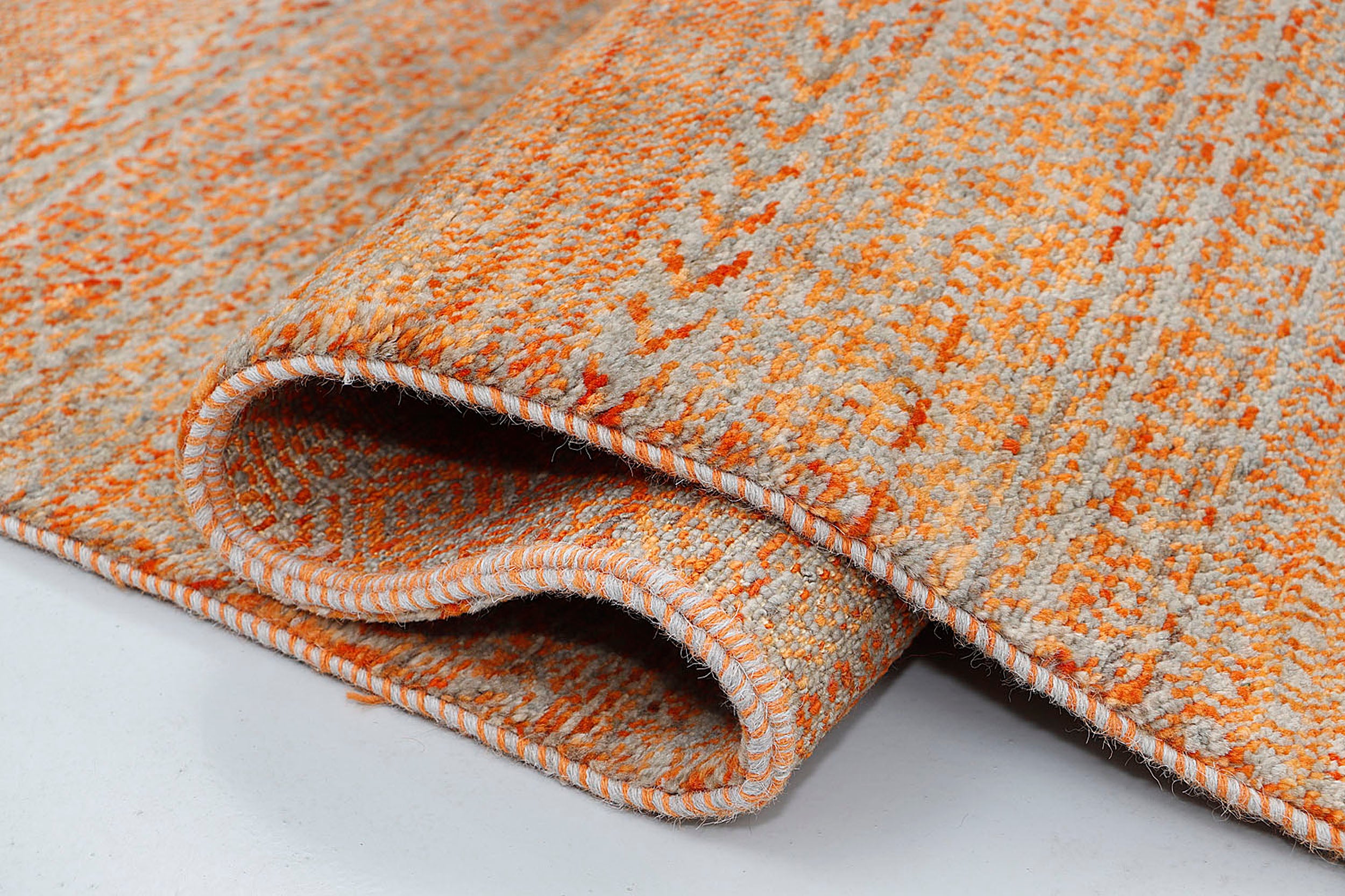 A high-resolution close-up highlighting the double-knot texture and the luminous, multi-tonal hues of variegated orange wool against a silver-grey backdrop.