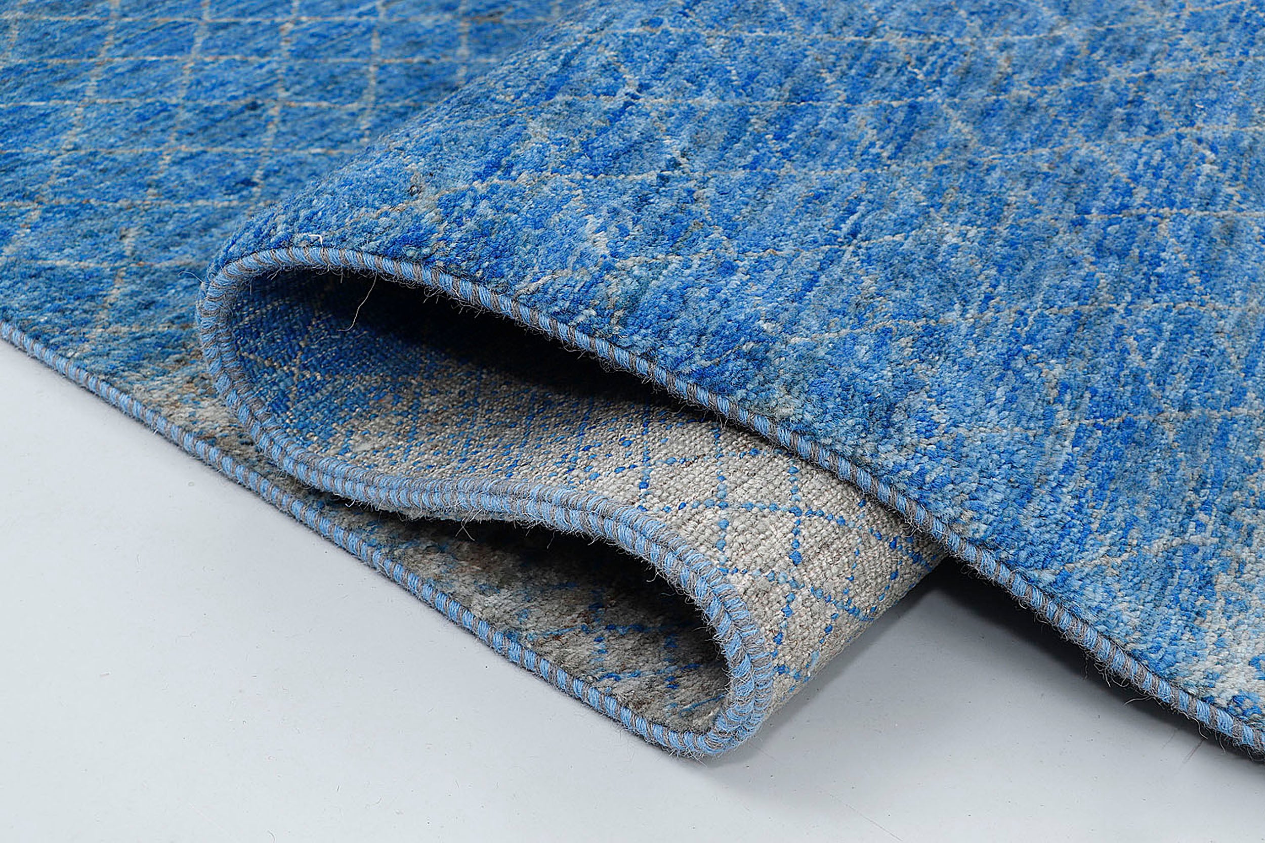 A close-up highlighting the double-knot construction and the unique ombré effect of the blue variegated wool against a shimmering silver background.
